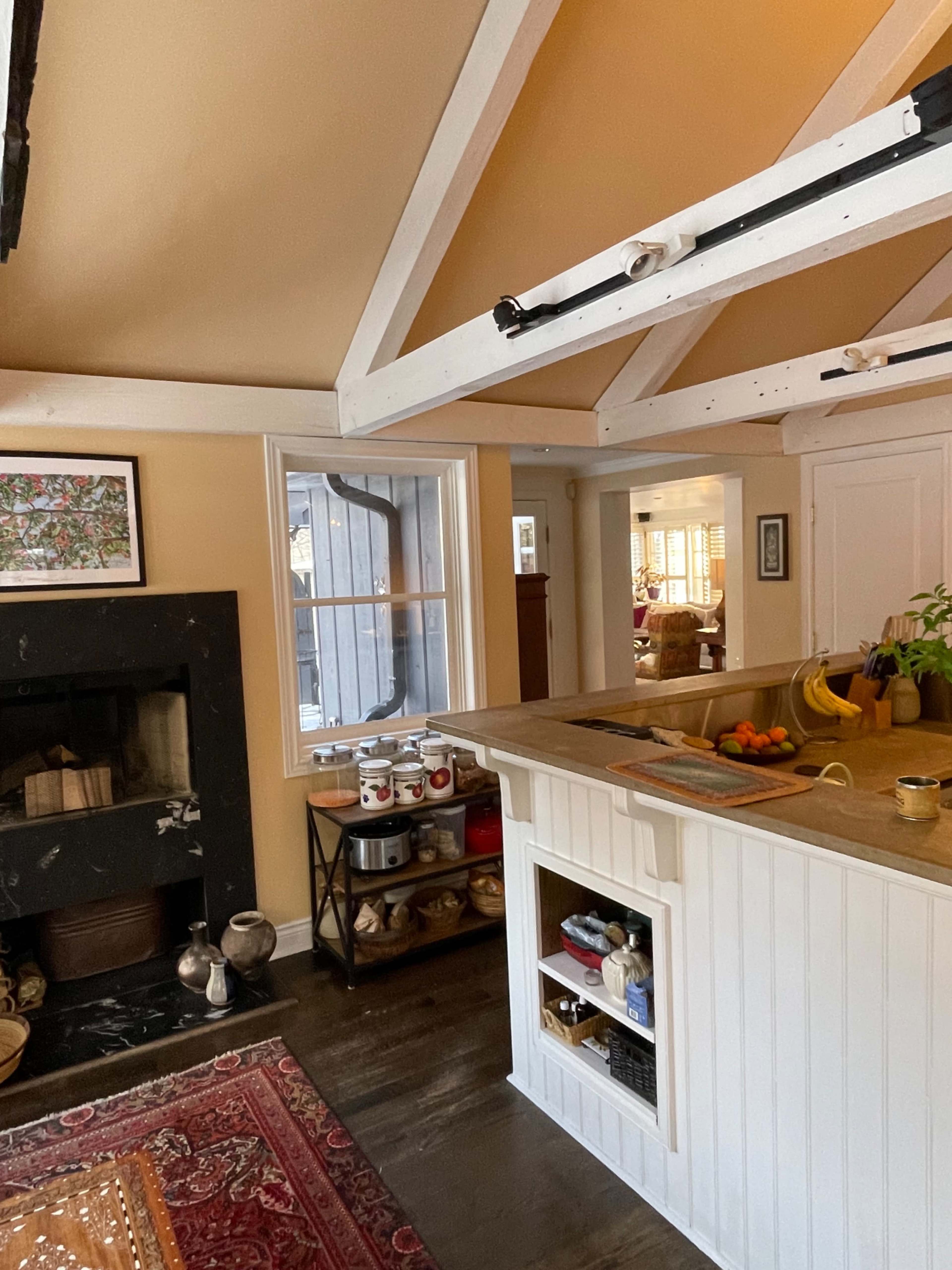A cozy kitchen with a wooden countertop, open shelving, a black fireplace, and a view into a living area through a window.