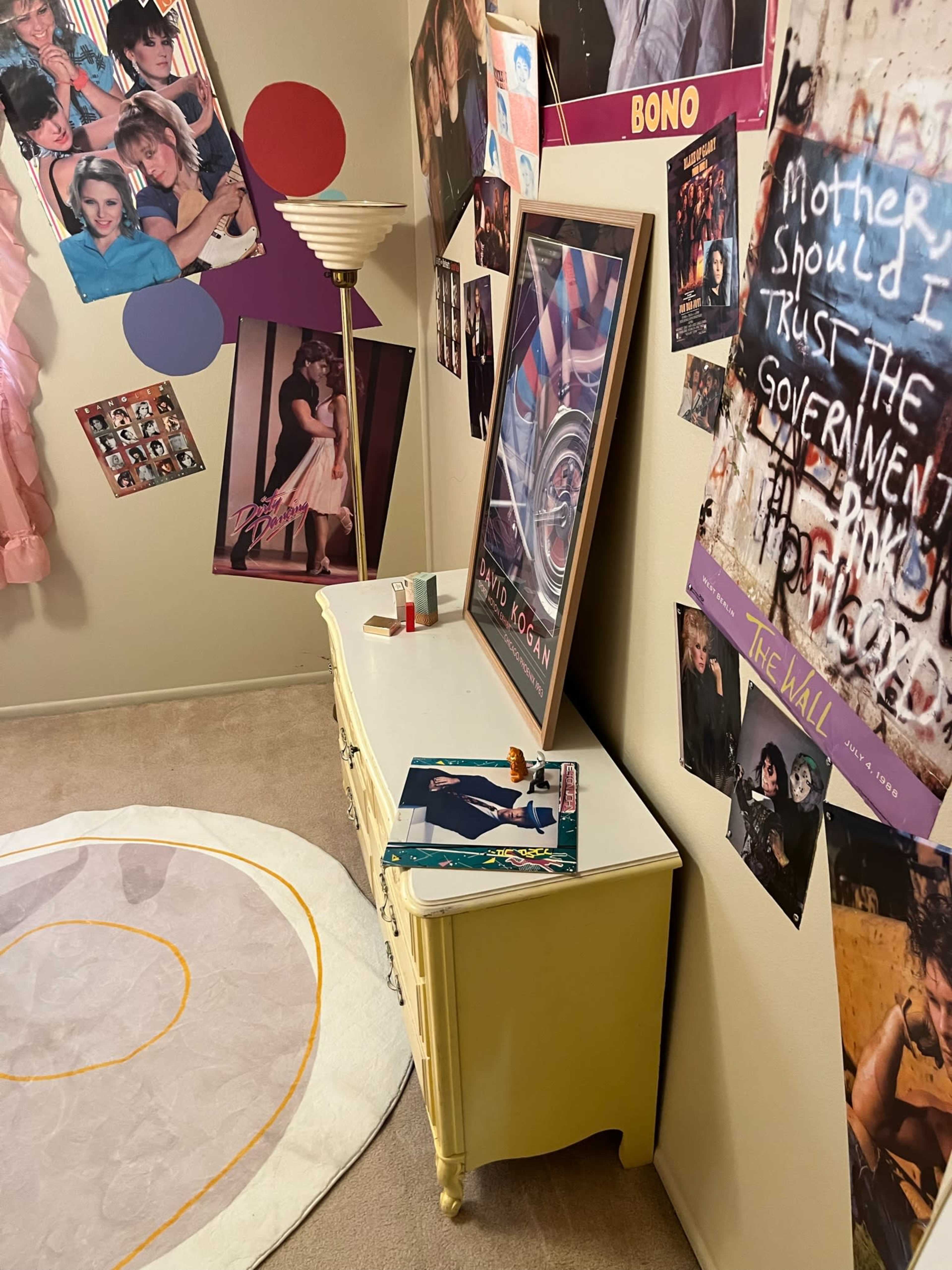 A room with posters of musicians on the walls, a vintage dresser, and a round rug on the floor.