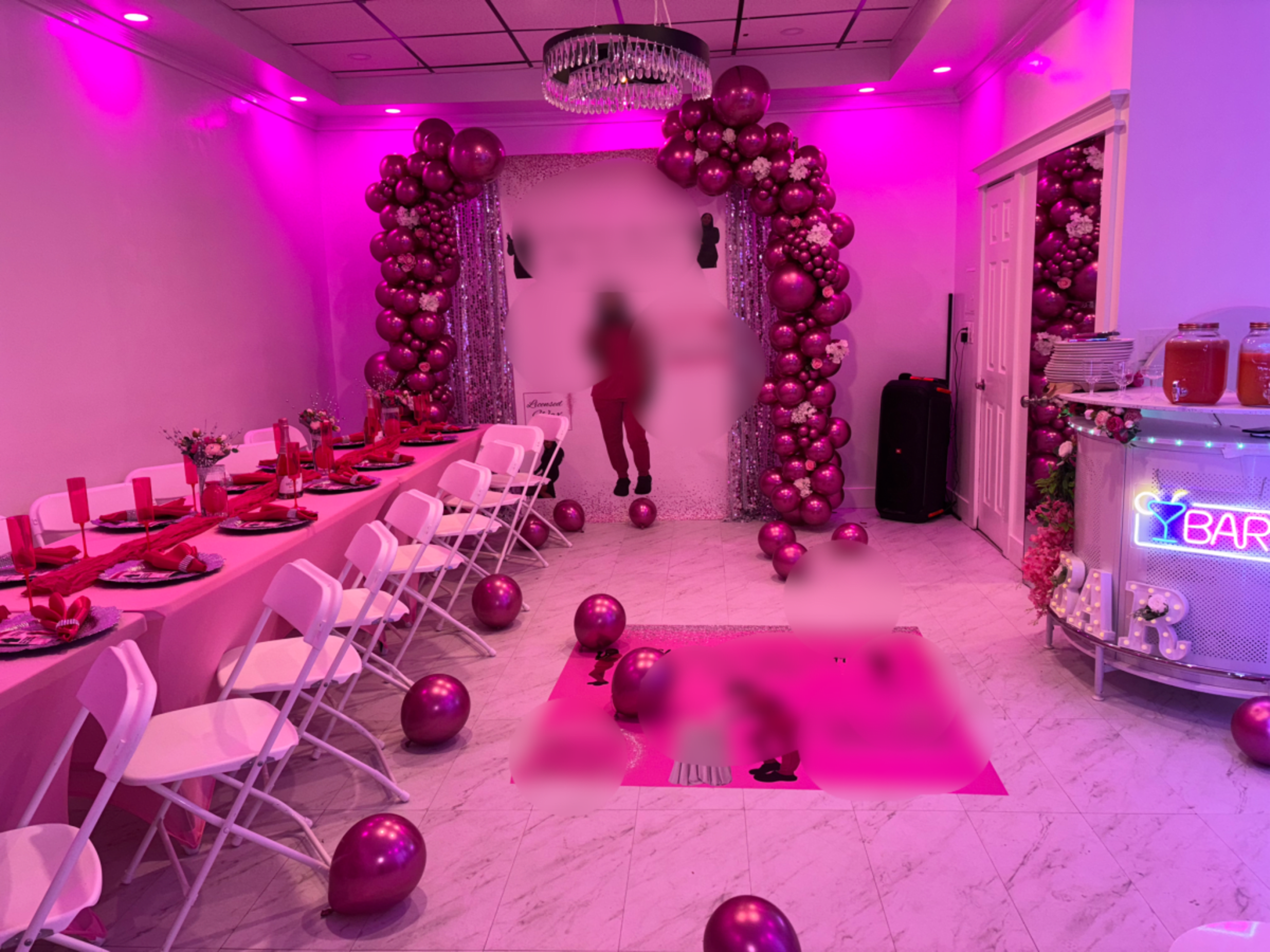 The image depicts a party venue decorated with pink balloons, a long table set for dining, and a sparkling backdrop.