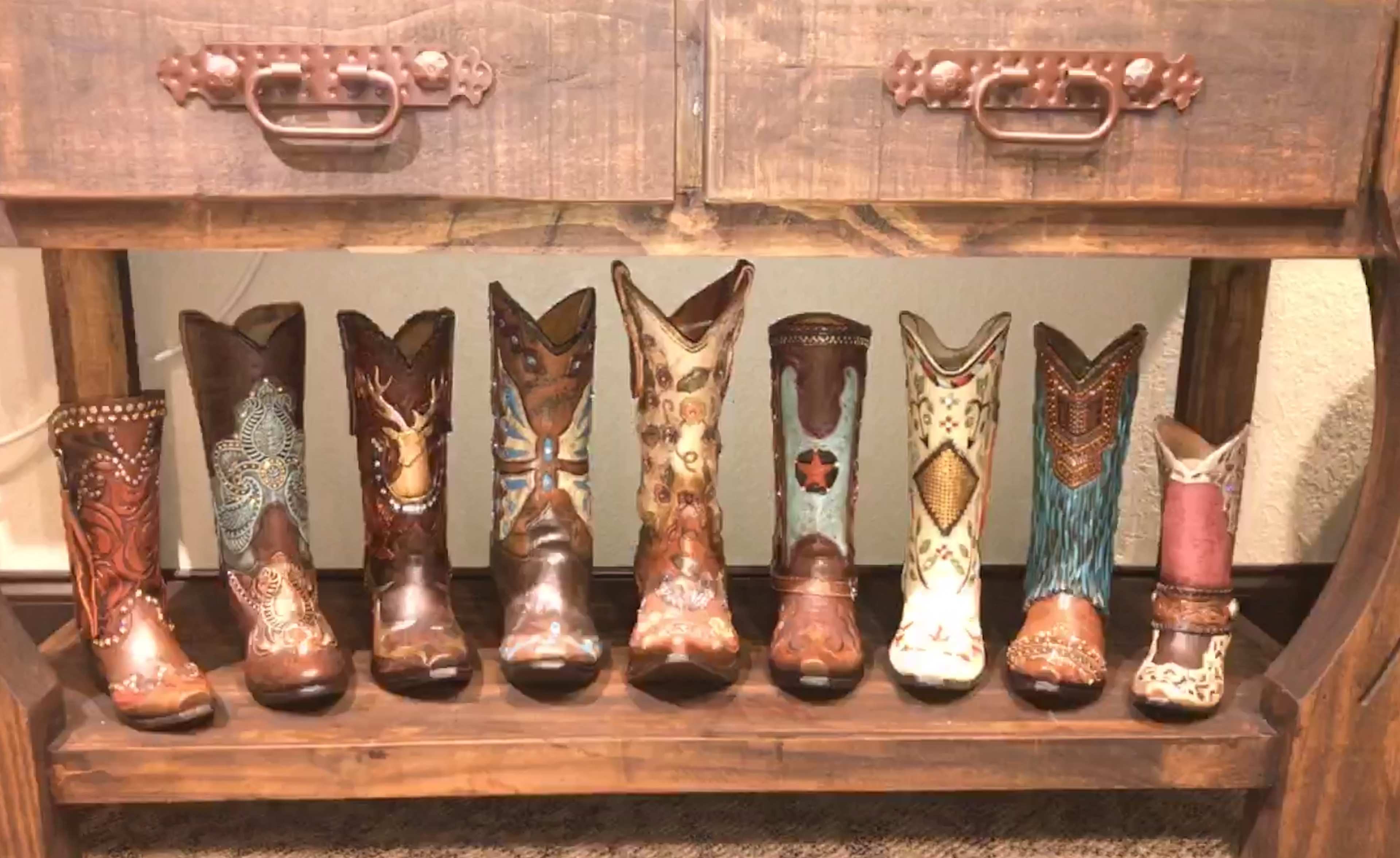 A row of decorative cowboy boots is displayed on a wooden shelf under a rustic cabinet.