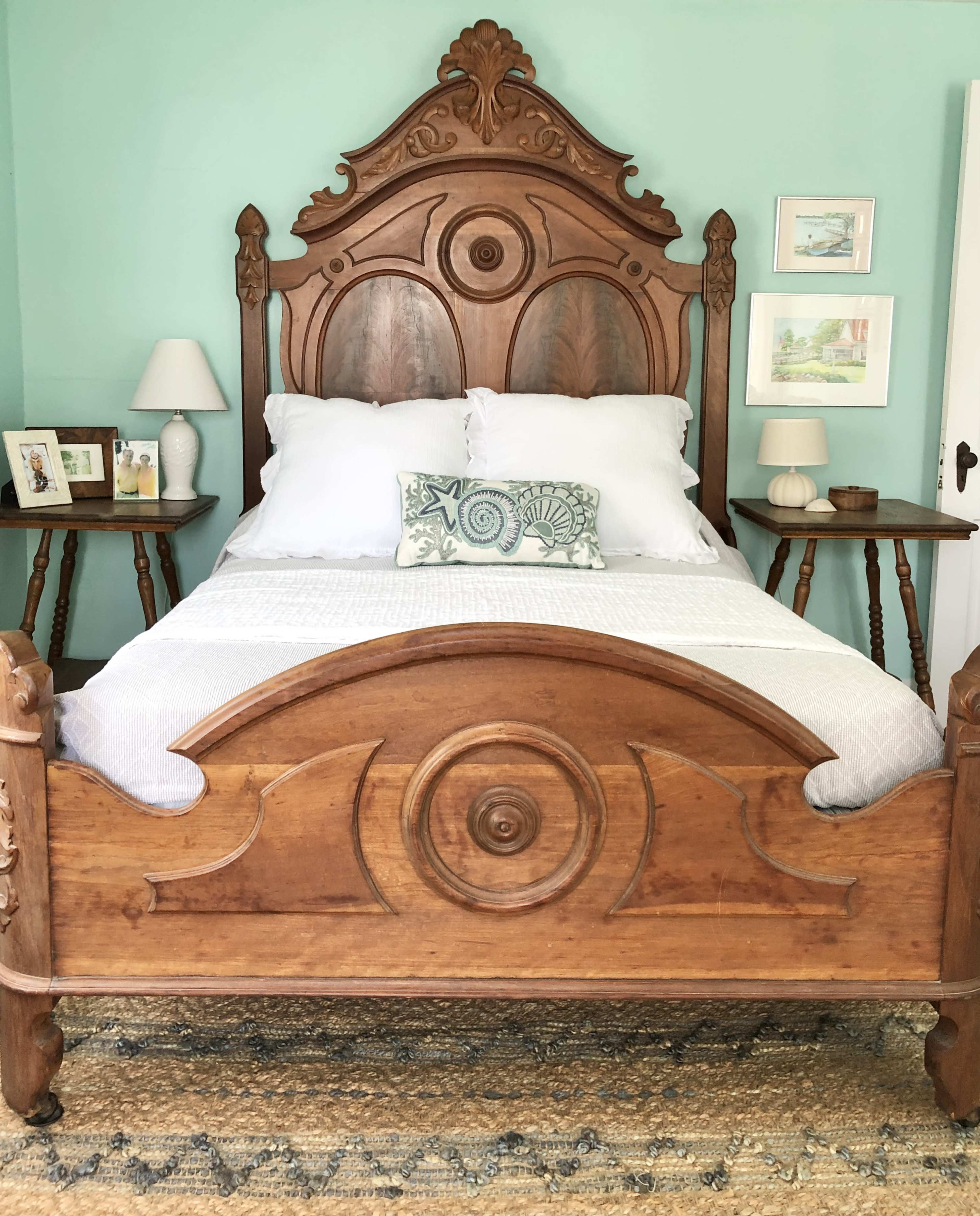 A wooden bed with a decorative headboard, white bedding, and matching lamps on either side, set against a light green wall.