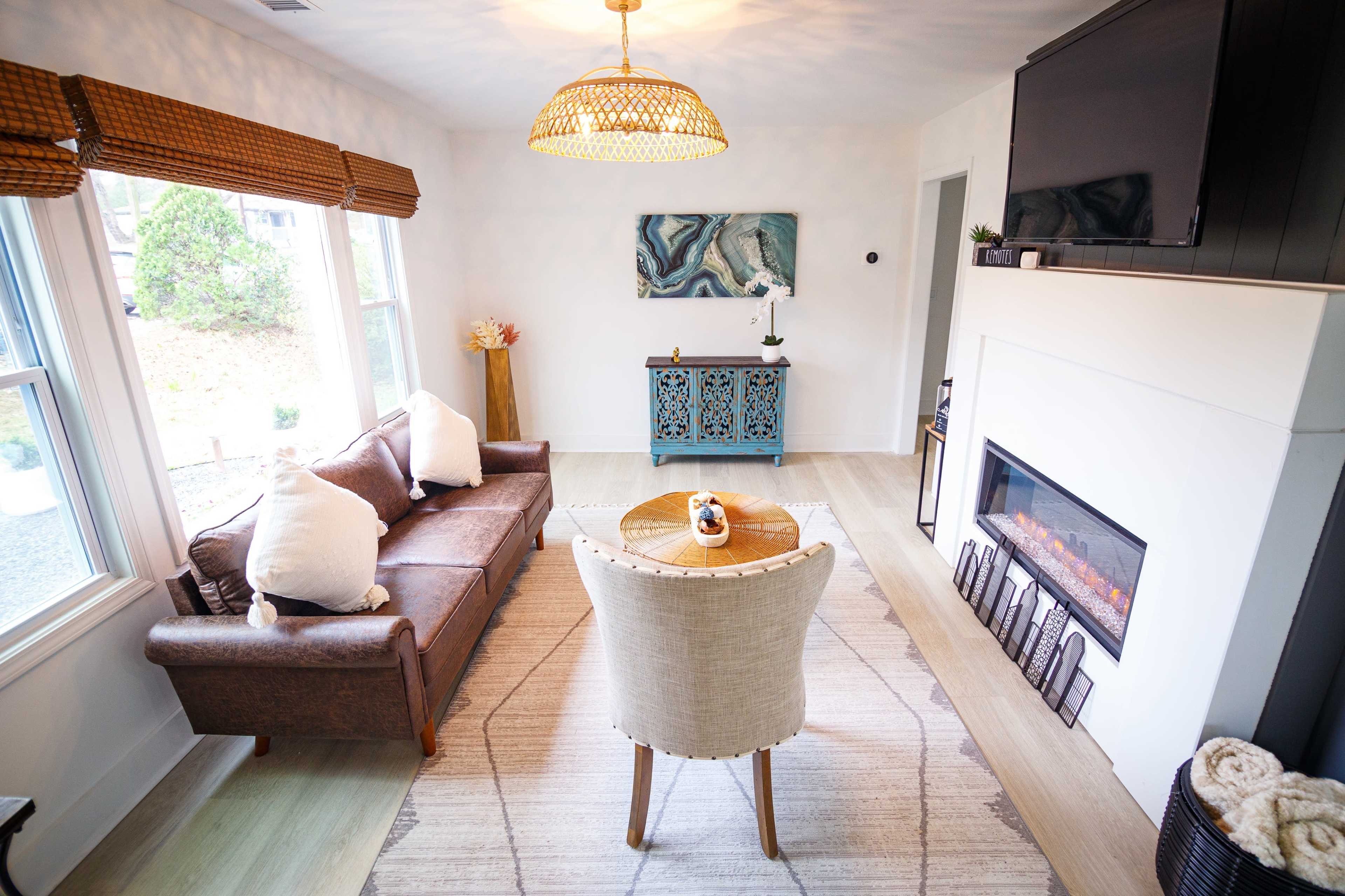 A living room features a brown leather sofa, a circular table with a decorative centerpiece, and a modern electric fireplace with a television mounted above it.
