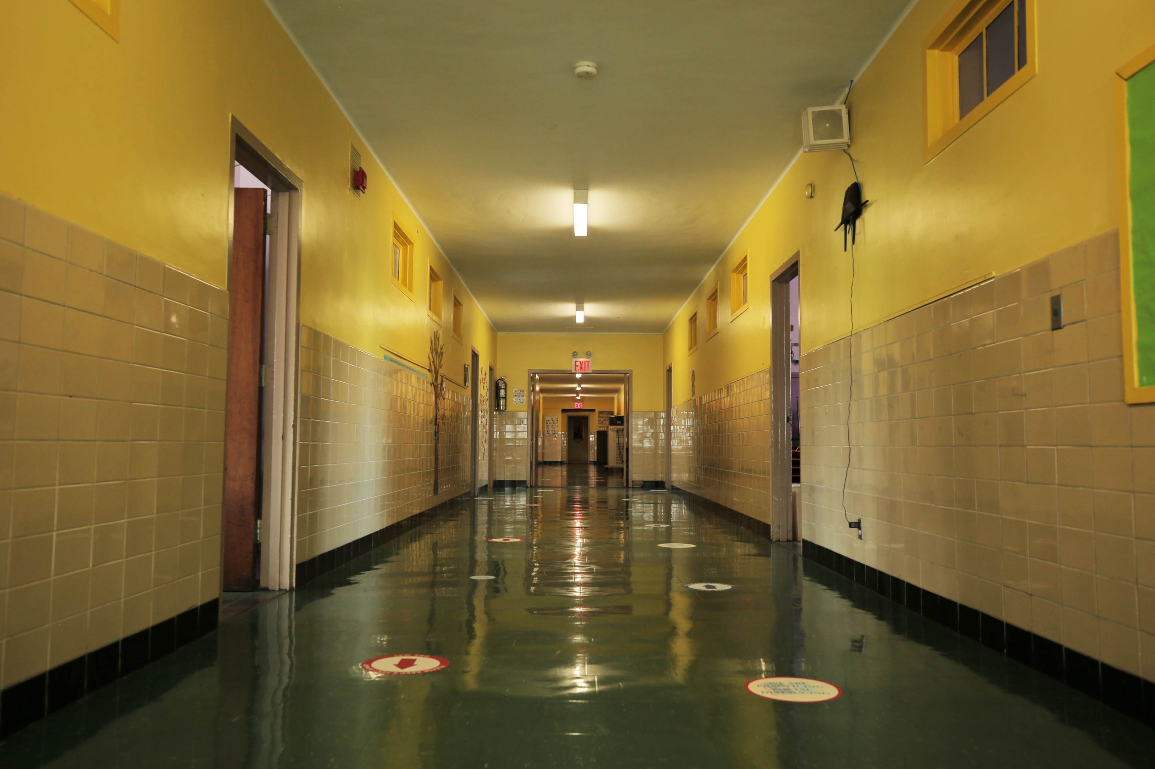 A long hallway is lined with yellow walls, featuring brown doors and a glossy green floor that reflects the overhead lights.