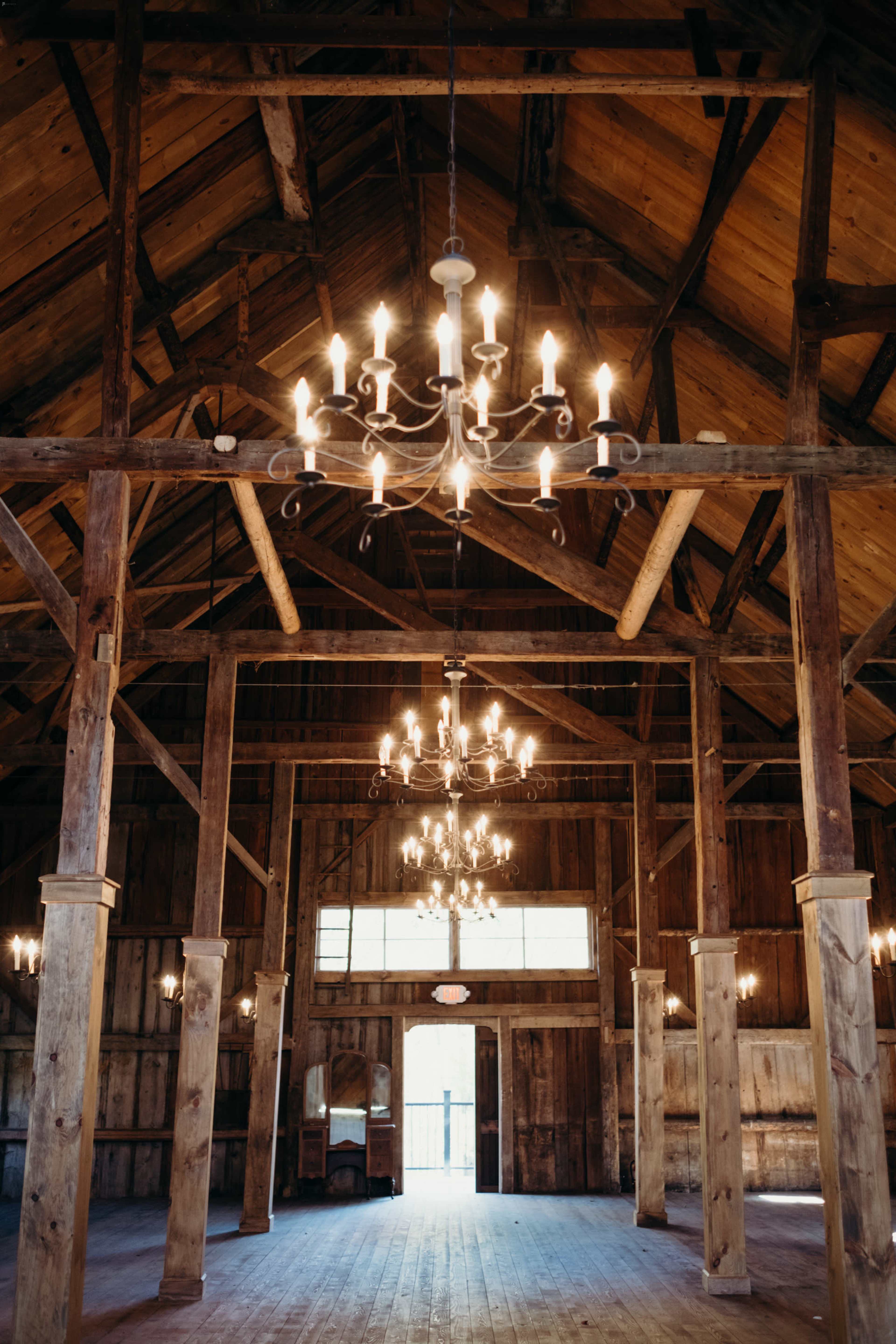 The interior of a rustic wooden hall features high ceilings supported by wooden beams and multiple chandeliers.
