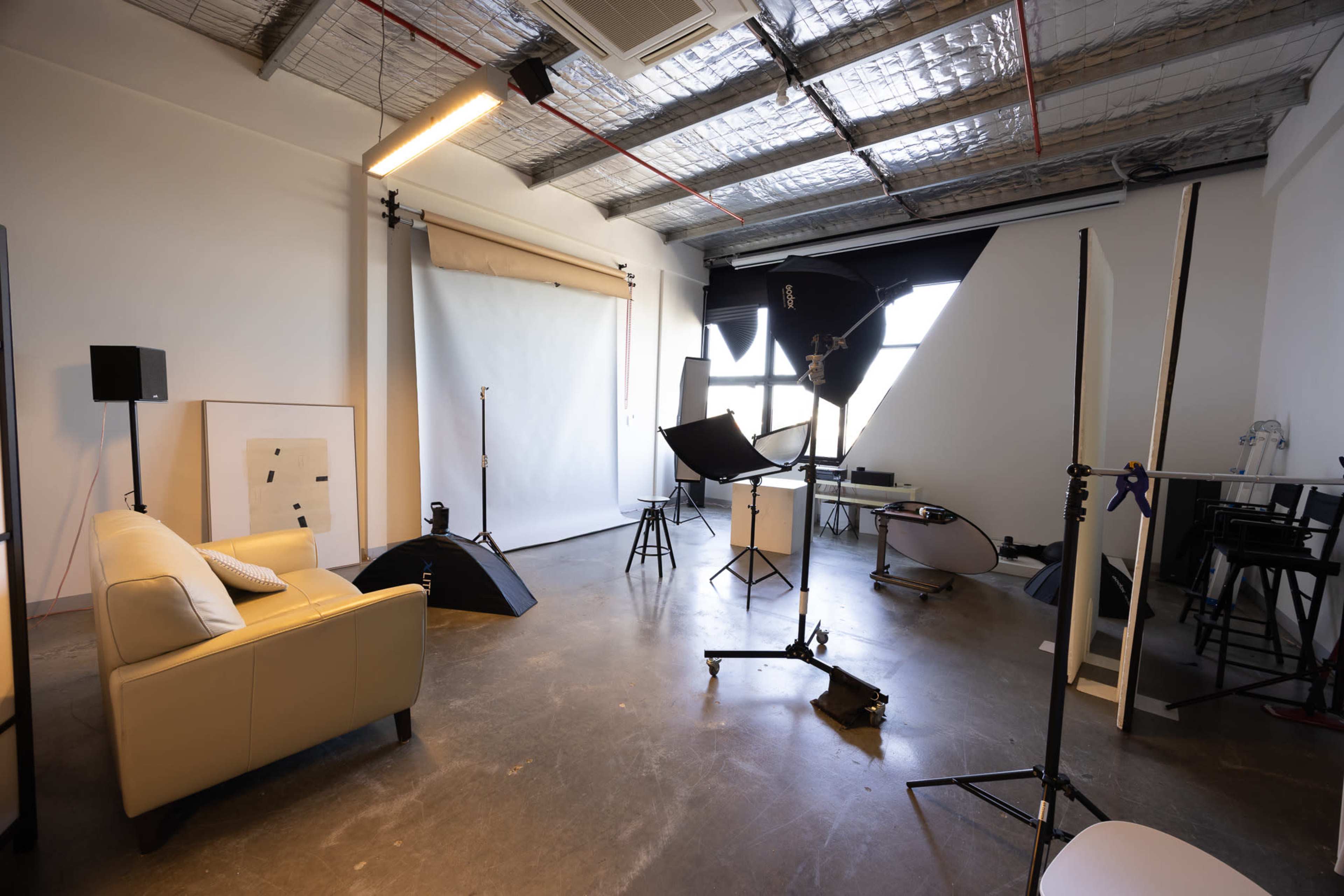 The image shows a photography studio with various equipment, including a backdrop, lighting setups, and seating areas.