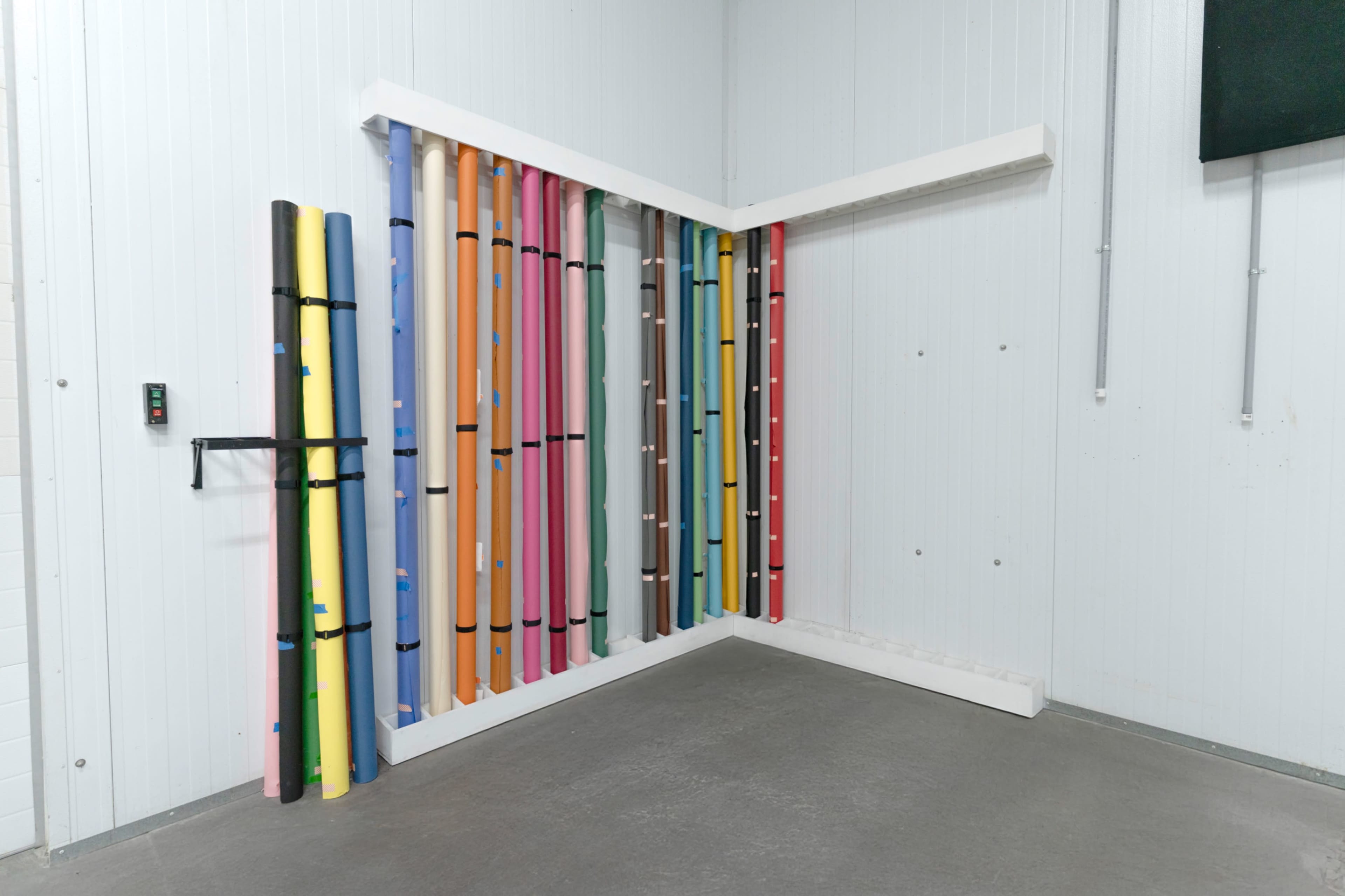 The image shows a corner of a room with several colorful rolled-up materials neatly arranged against the wall.