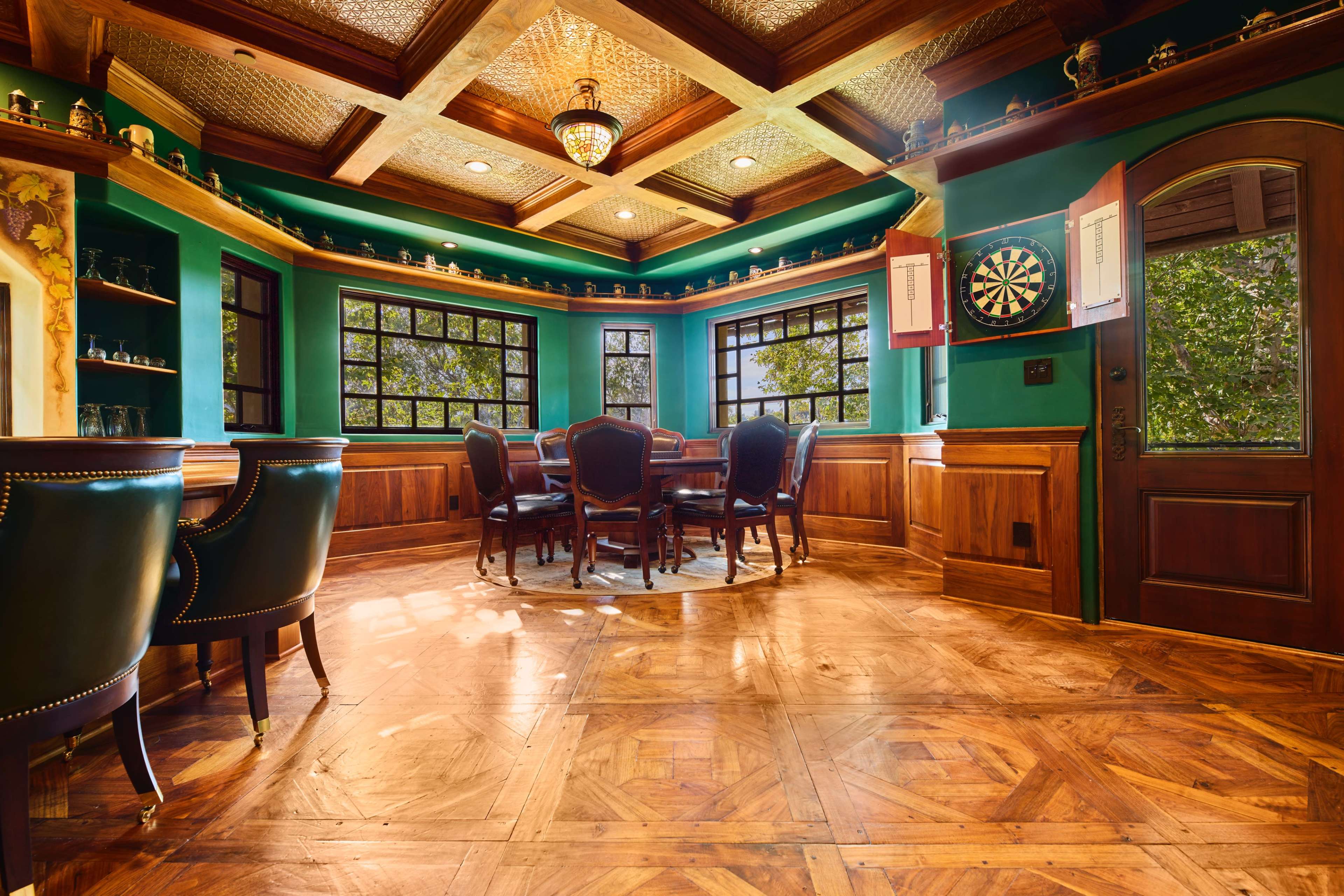 A cozy game room with a wooden table surrounded by chairs, dartboard on the wall, and large windows letting in natural light.