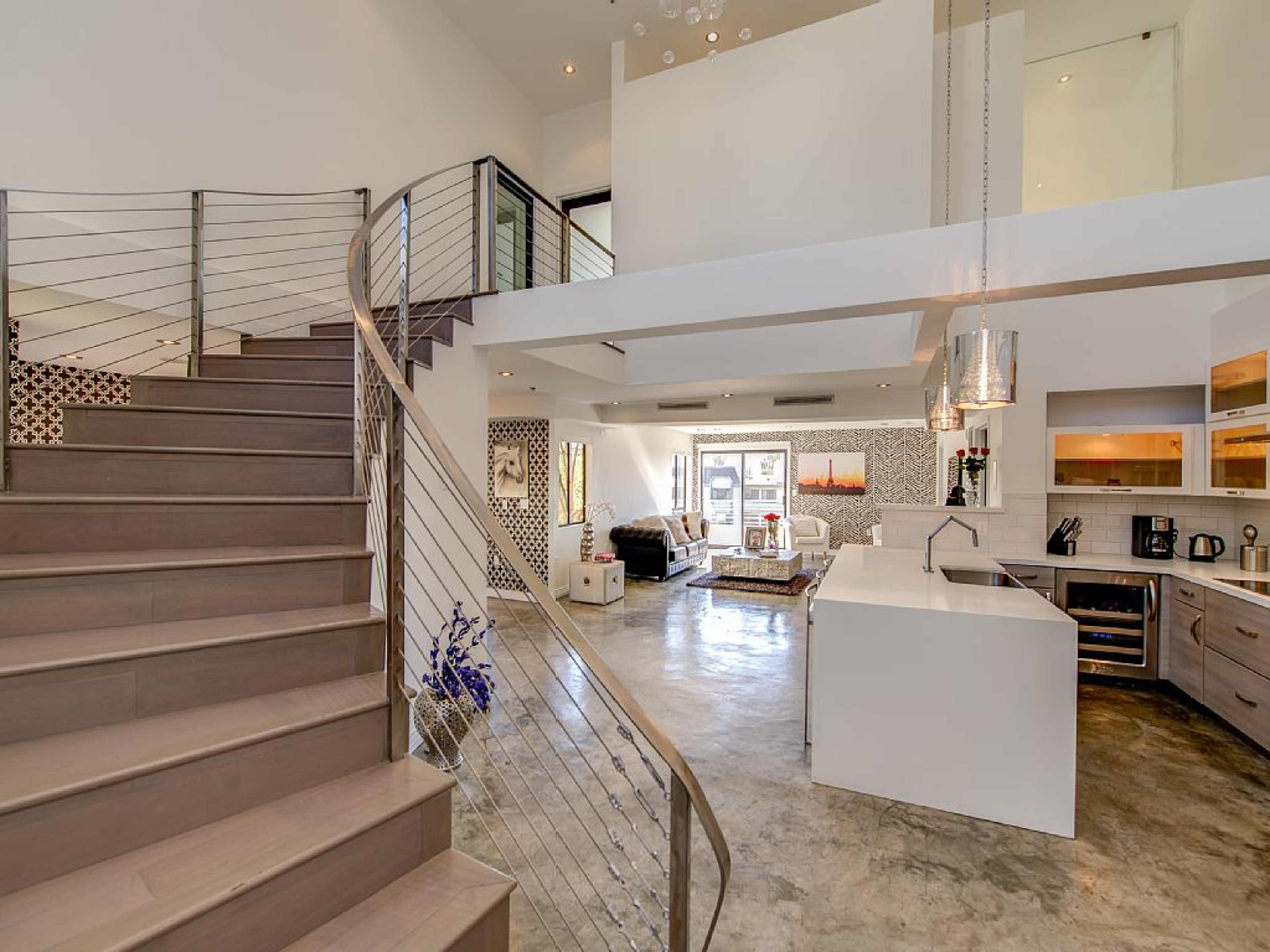 A modern open-concept living space features a spiral staircase, a sleek kitchen, and large windows allowing natural light to fill the area.