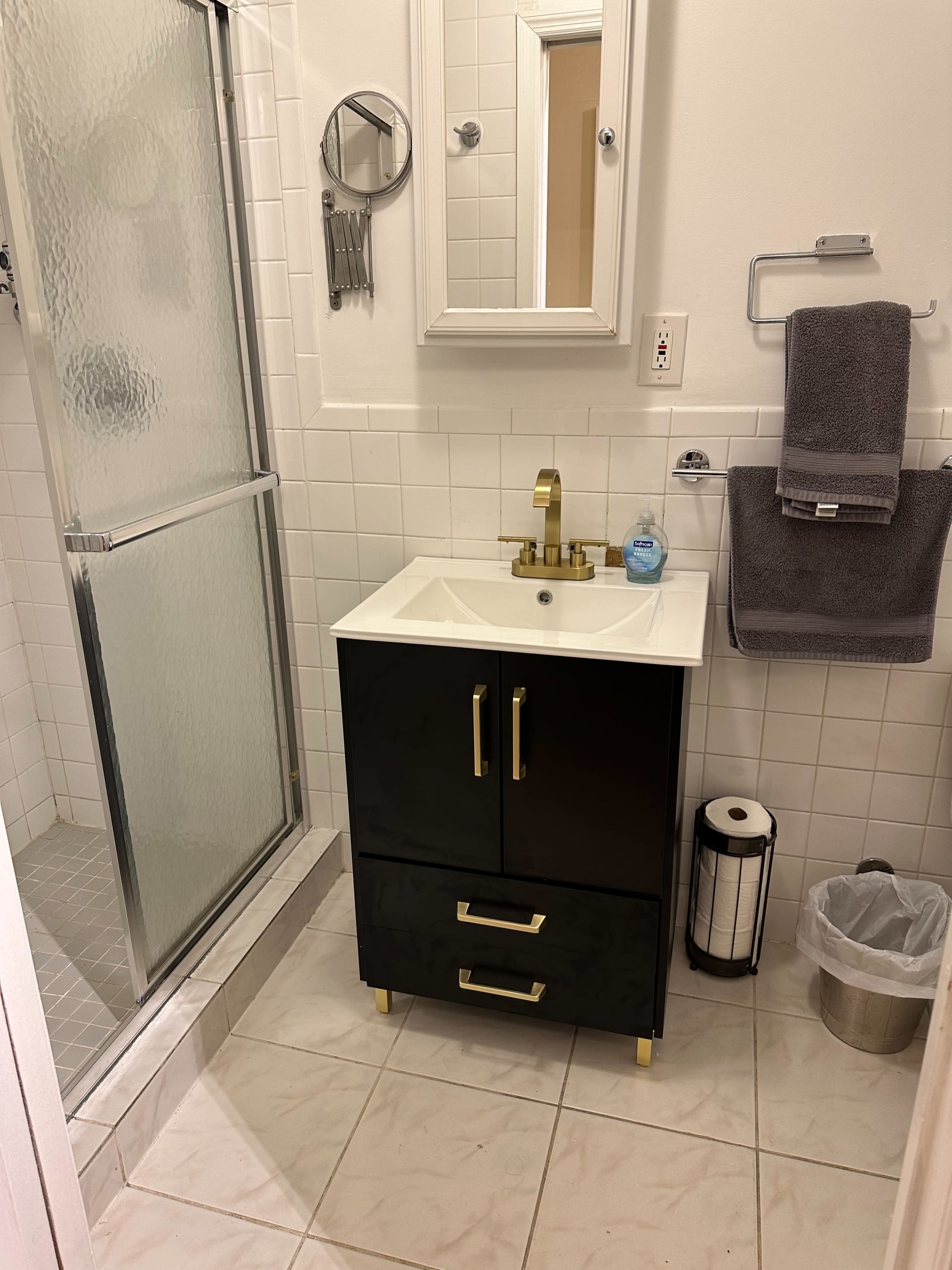 The image shows a modern bathroom featuring a black vanity with a sink, a mirror above it, a shower area with a glass door, and neatly arranged towels and accessories.