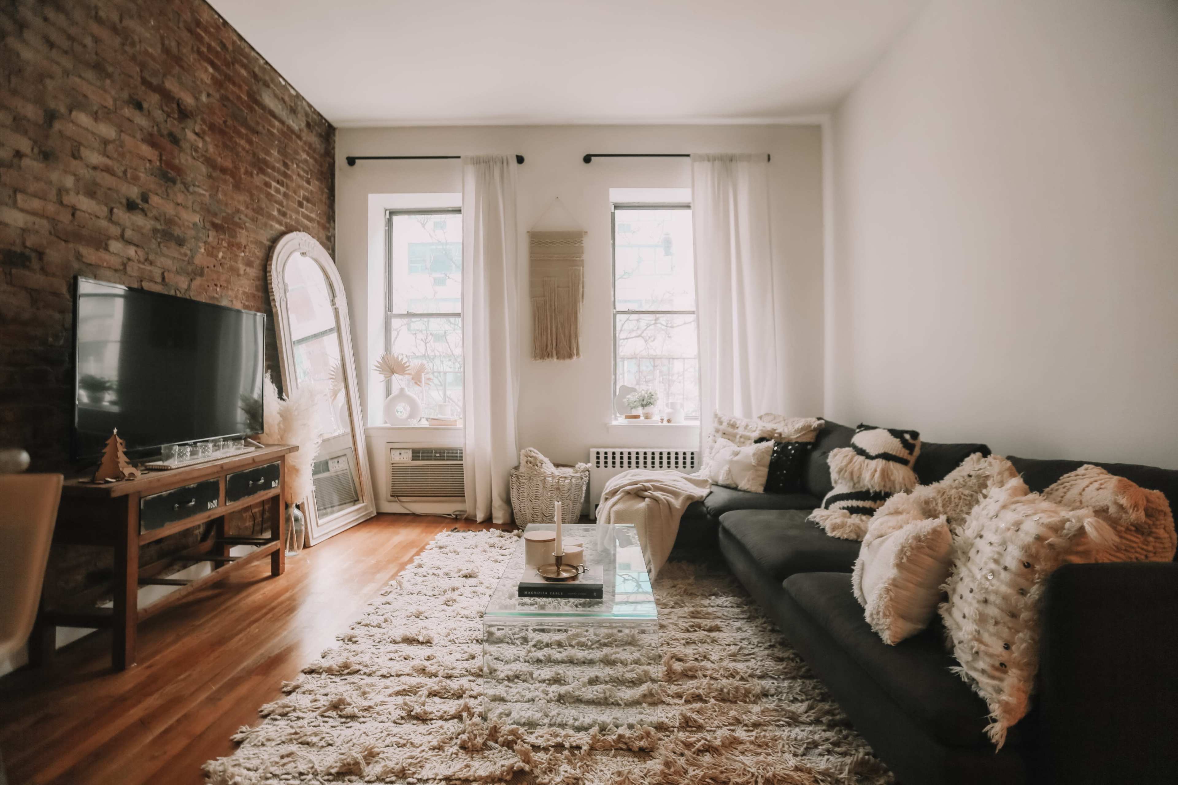 A cozy living room with a brick wall, a large television, and a dark sofa adorned with decorative pillows, set on a plush rug.