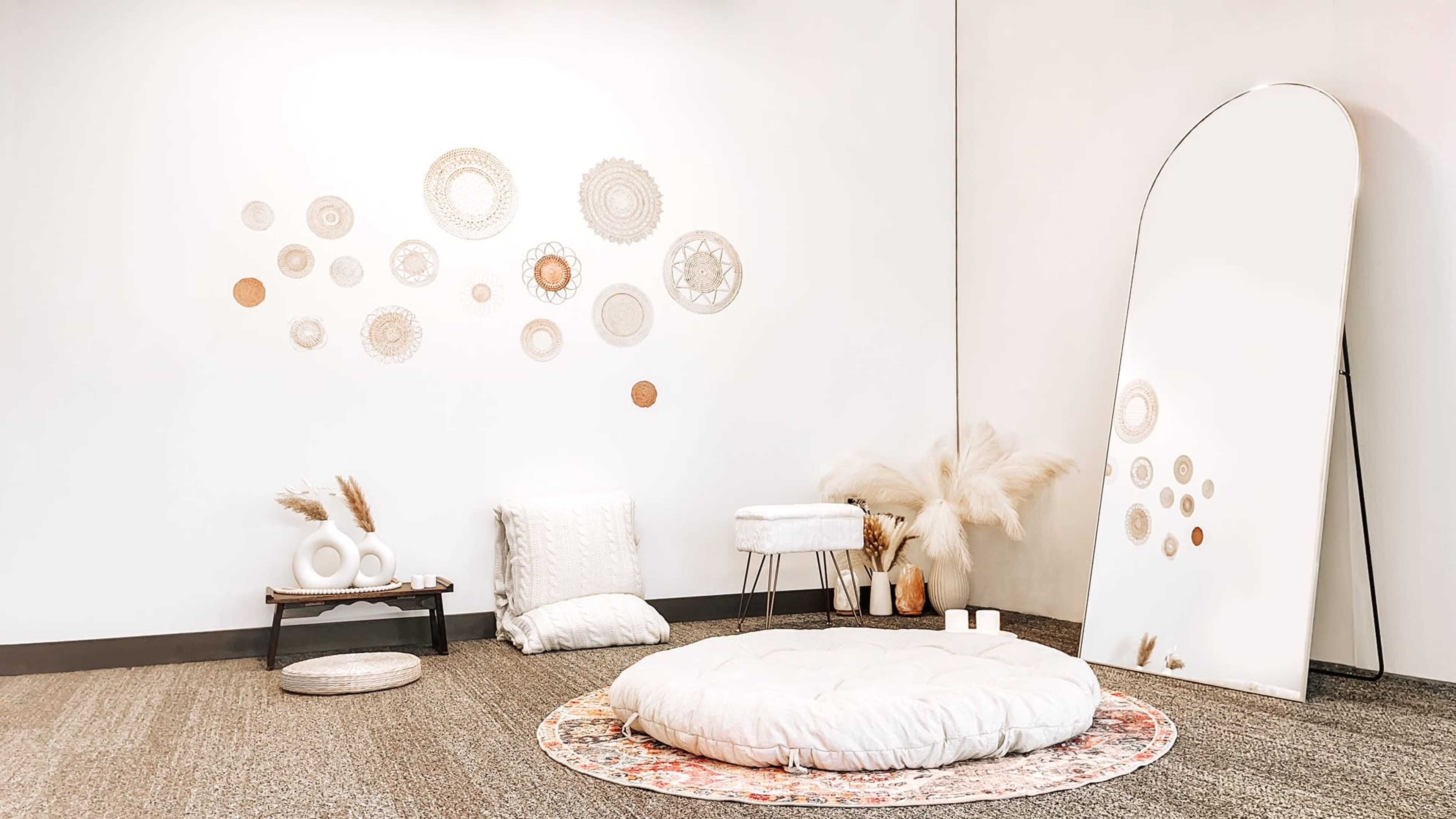 A minimalist room with a large round floor cushion, a decorative mirror, and a wall adorned with circular wall art.