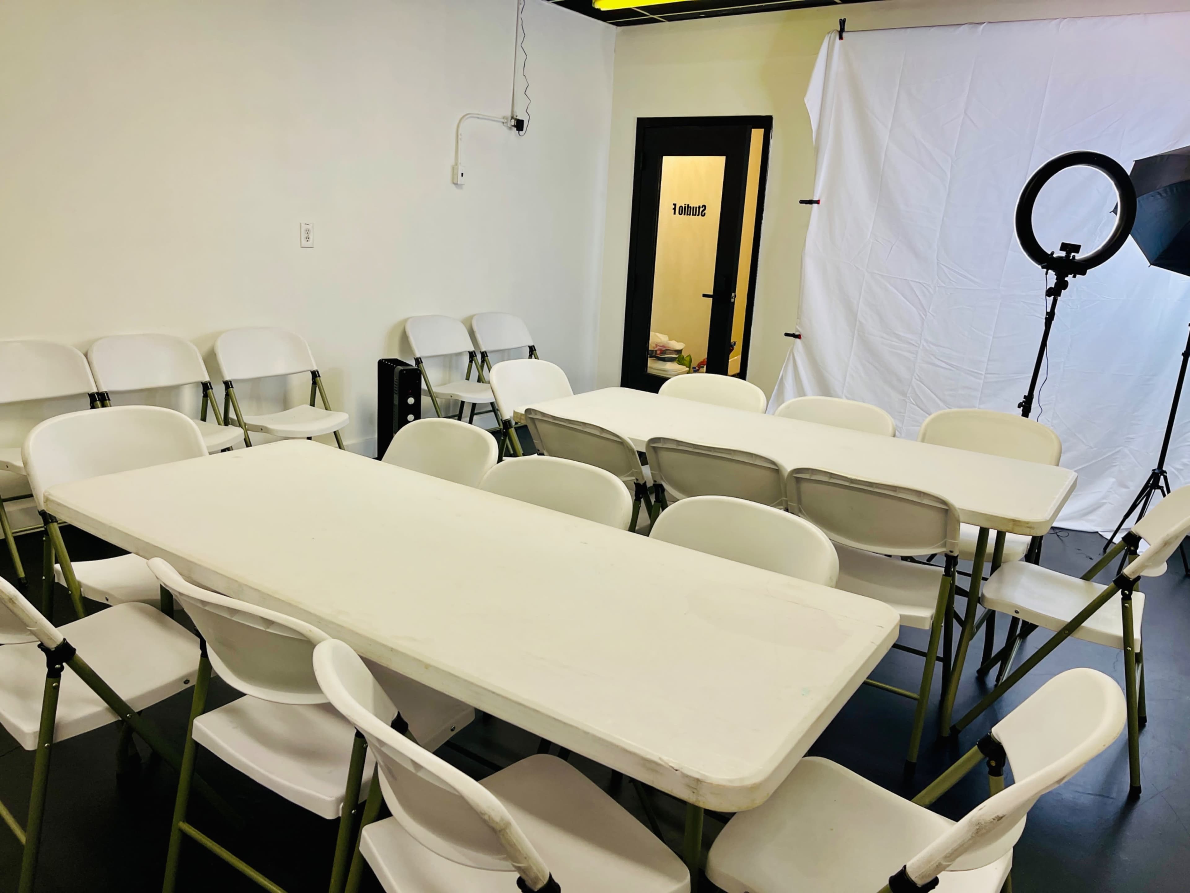 A room with a large table surrounded by folding chairs, with a backdrop and lighting equipment set up nearby.