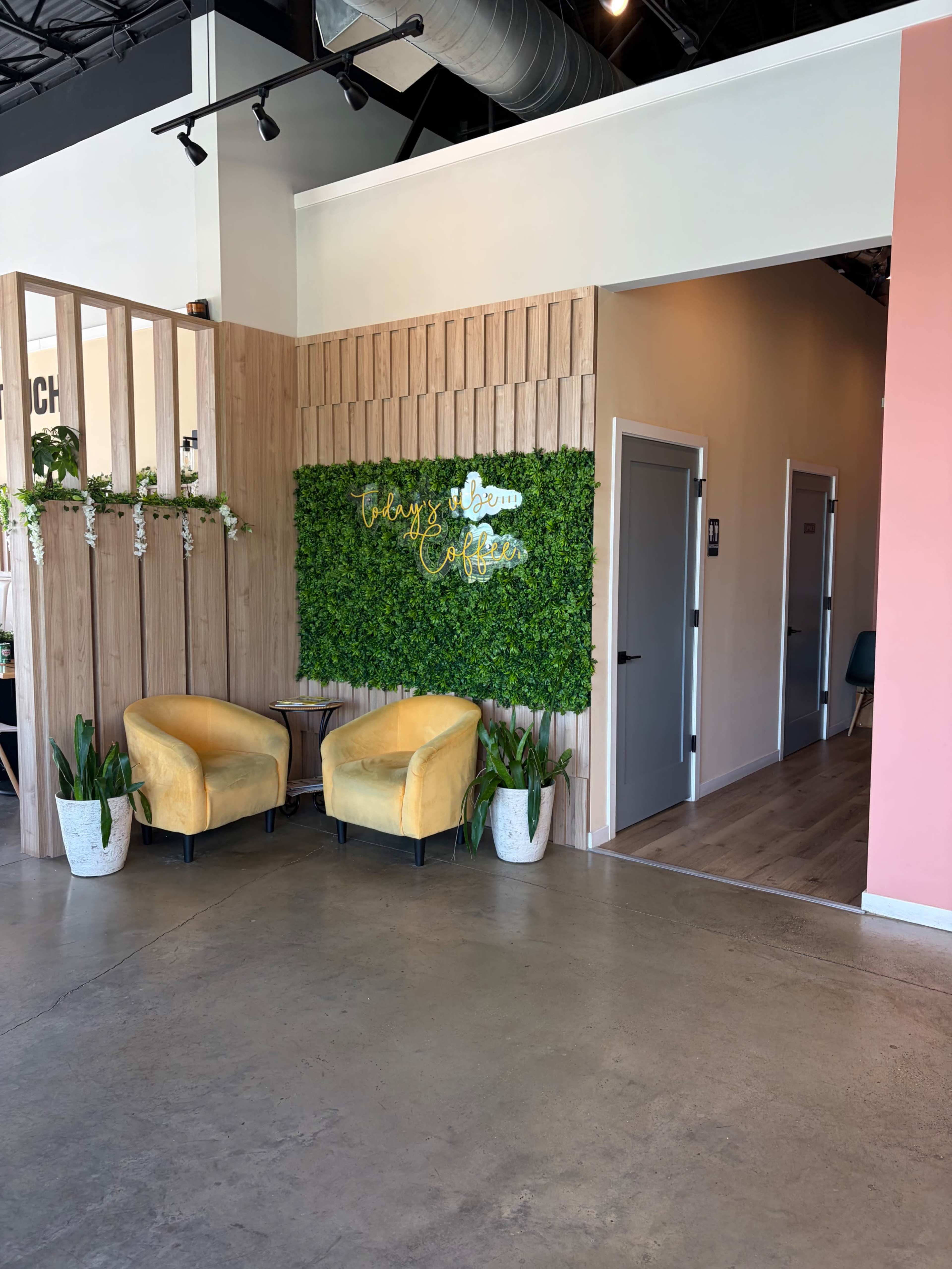 The image shows a modern interior space with two yellow armchairs, a green wall with decorative lettering, and a corridor leading to additional rooms.