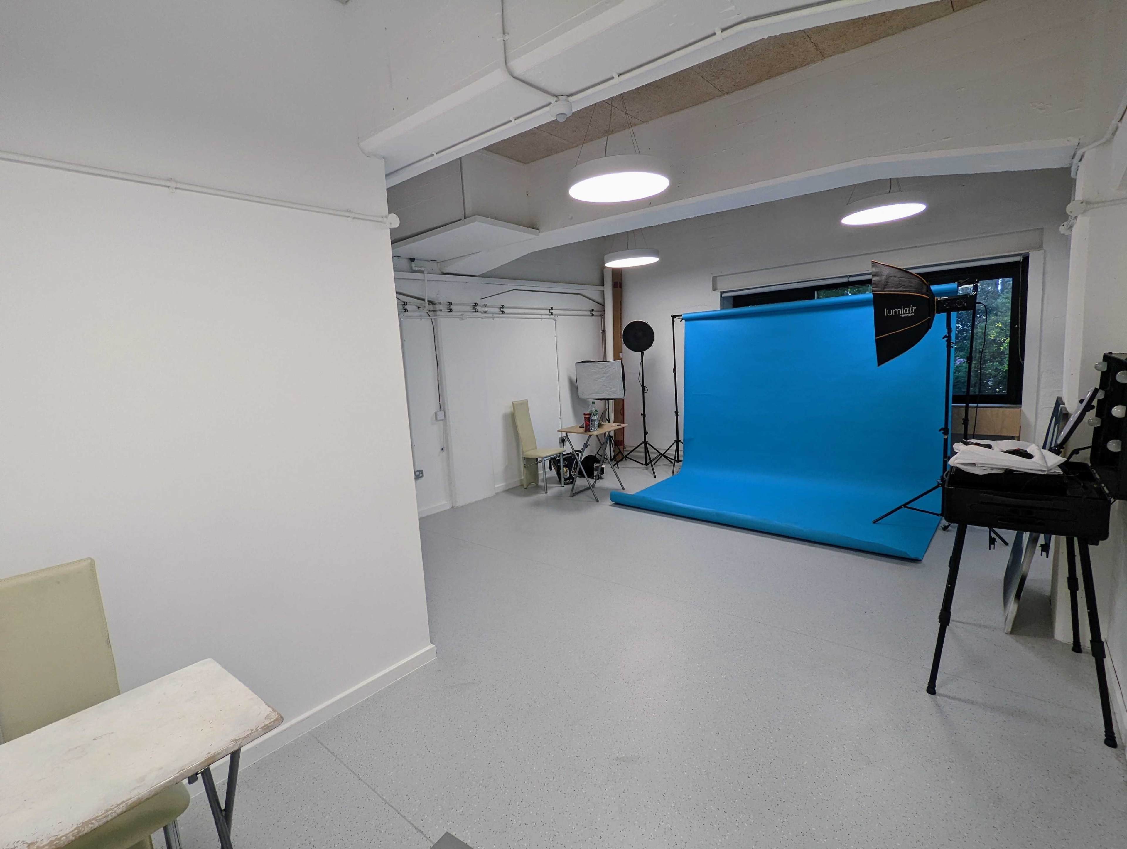 A well-lit studio space featuring a blue backdrop, photography equipment, and a table with chairs.