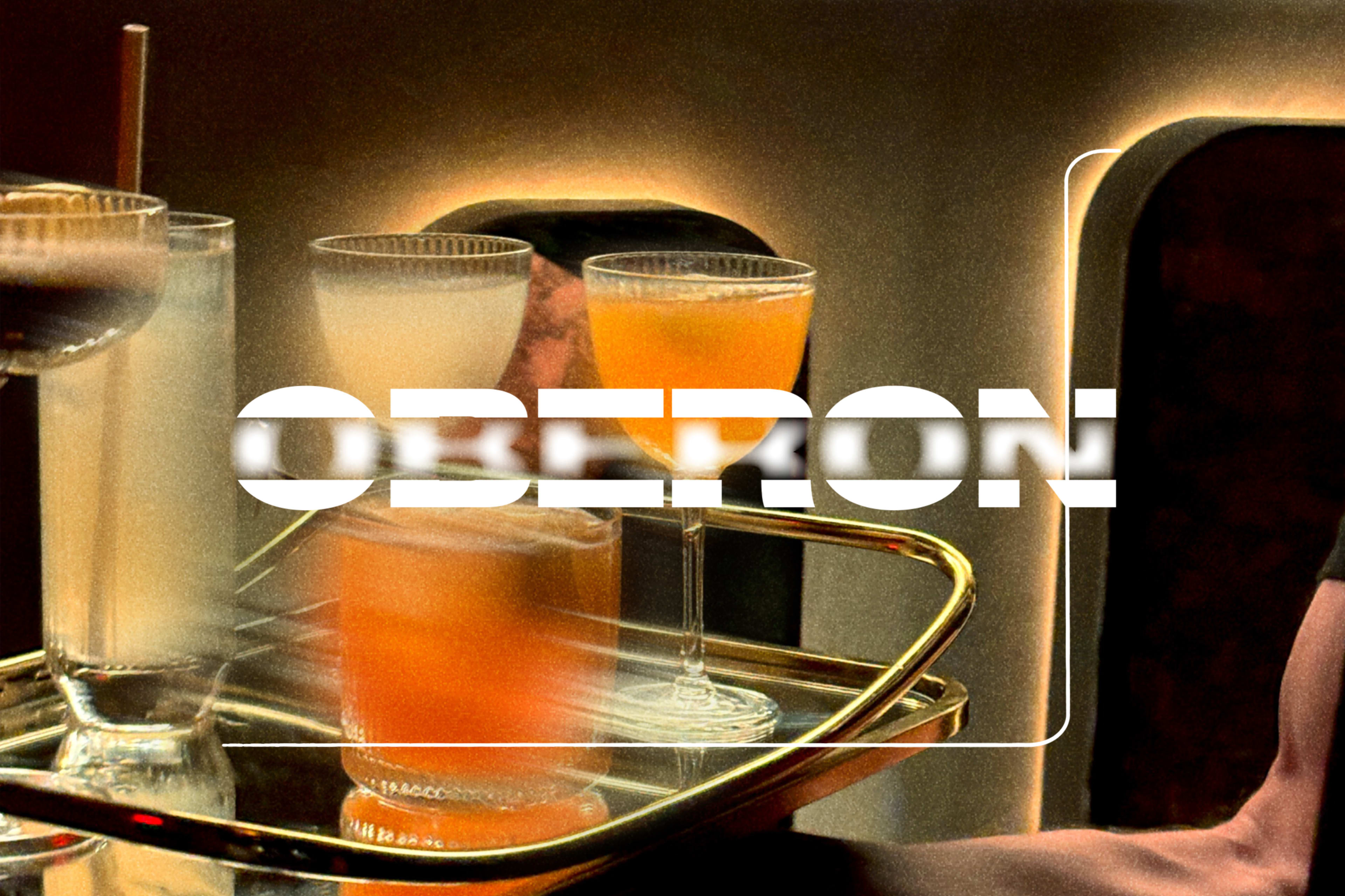 A tray holds four cocktails, each in distinct glasses, with a bold text overlay reading "OBERON."