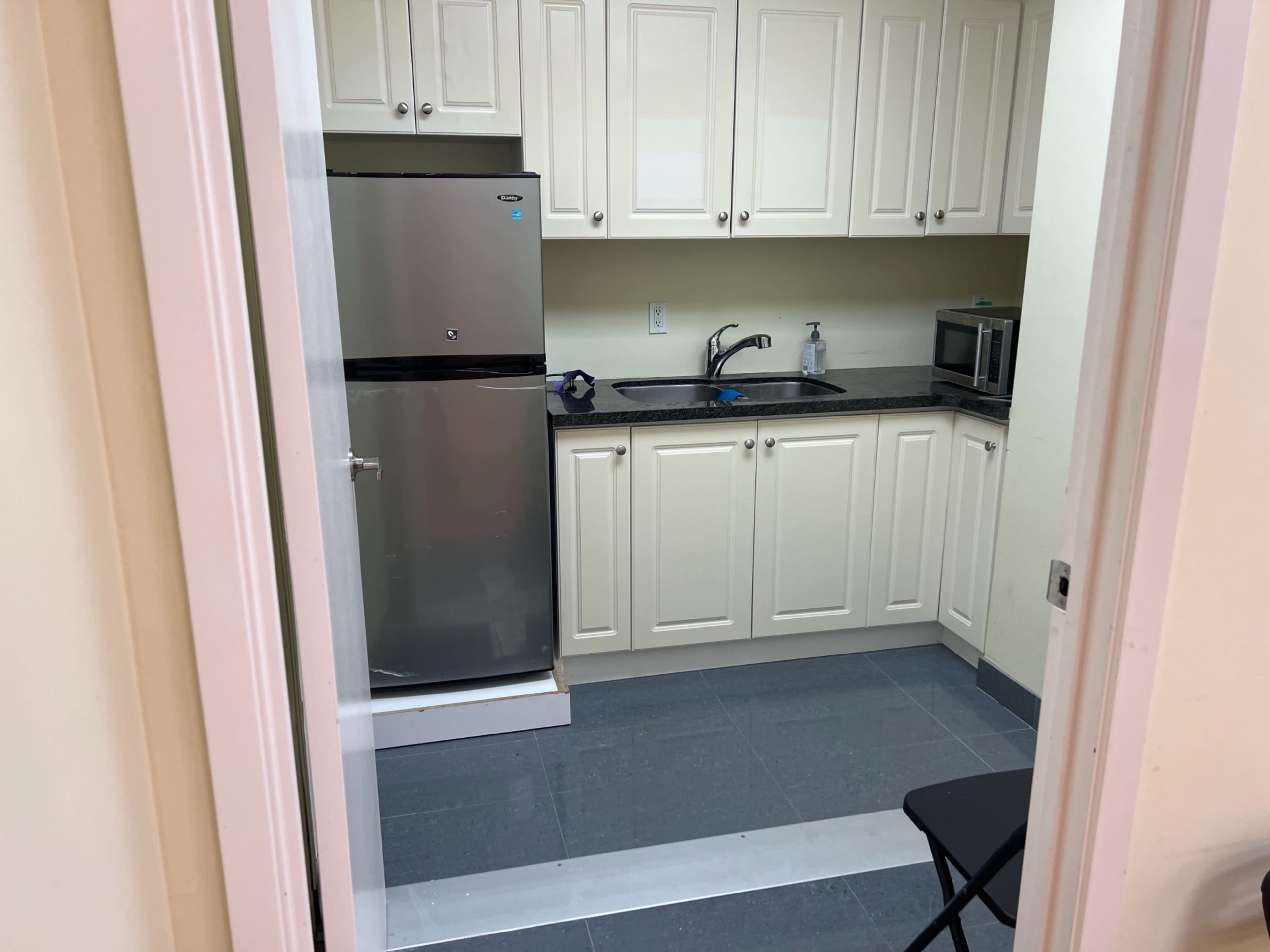 A small kitchen area featuring a refrigerator, sink, microwave, and cabinetry against light-colored walls.