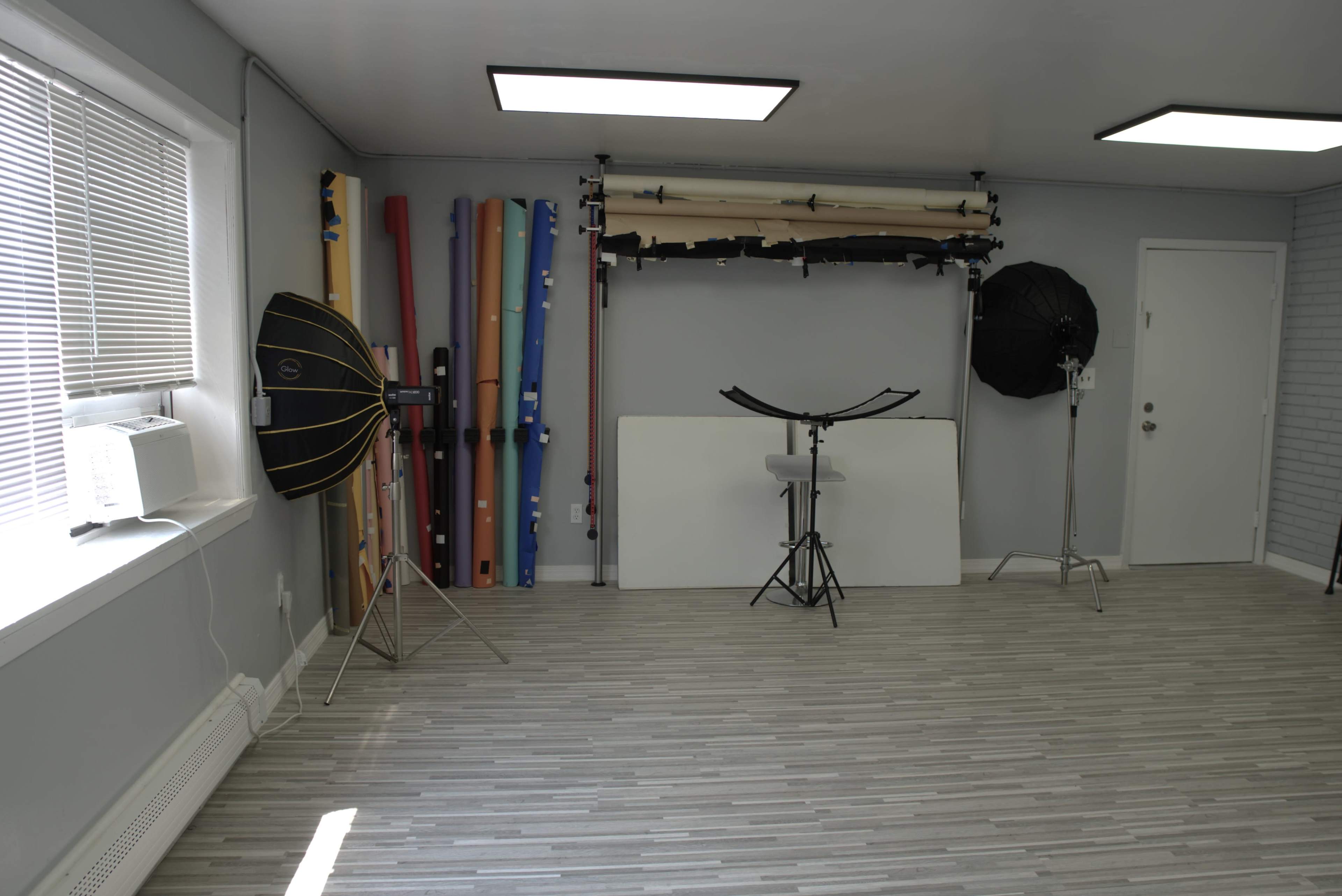 A photography studio featuring various colorful backdrops, lighting equipment, and a large white backdrop on the floor.