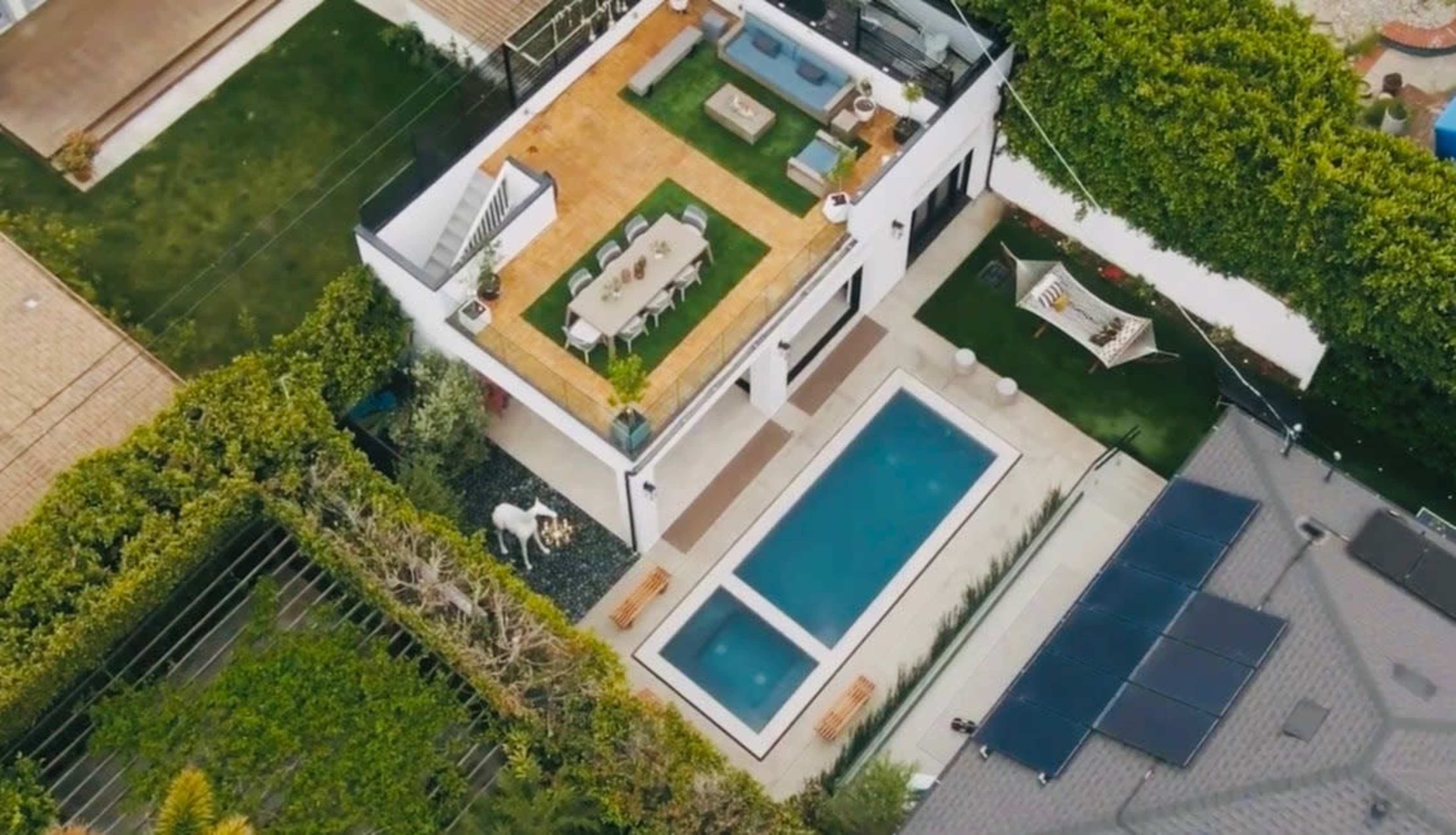 An aerial view of a modern house features a pool, a patio with seating, and landscaped gardens.