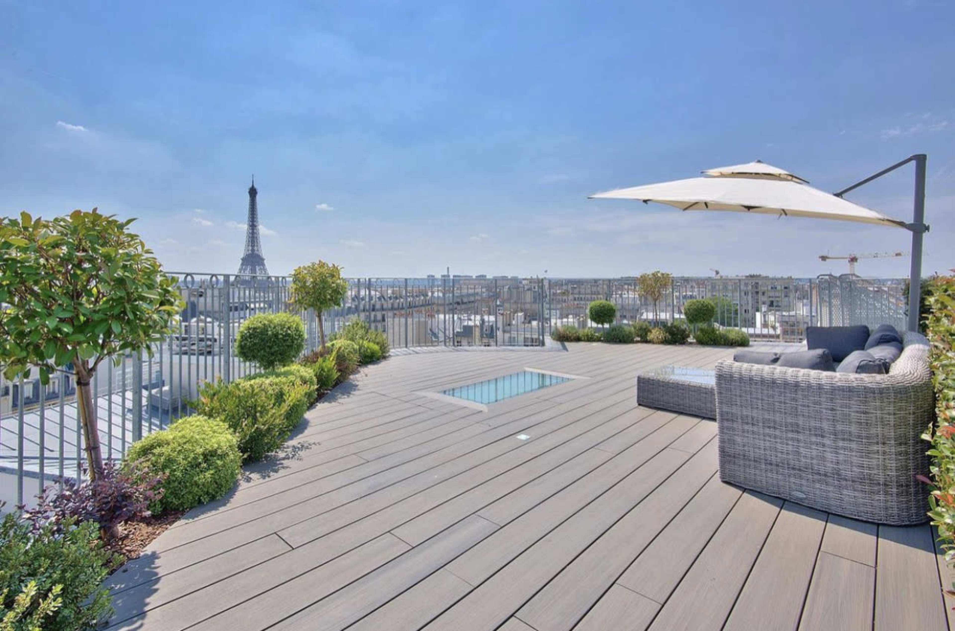 A rooftop terrace with a small swimming pool, lounge furniture, and a view of the Eiffel Tower in the background.