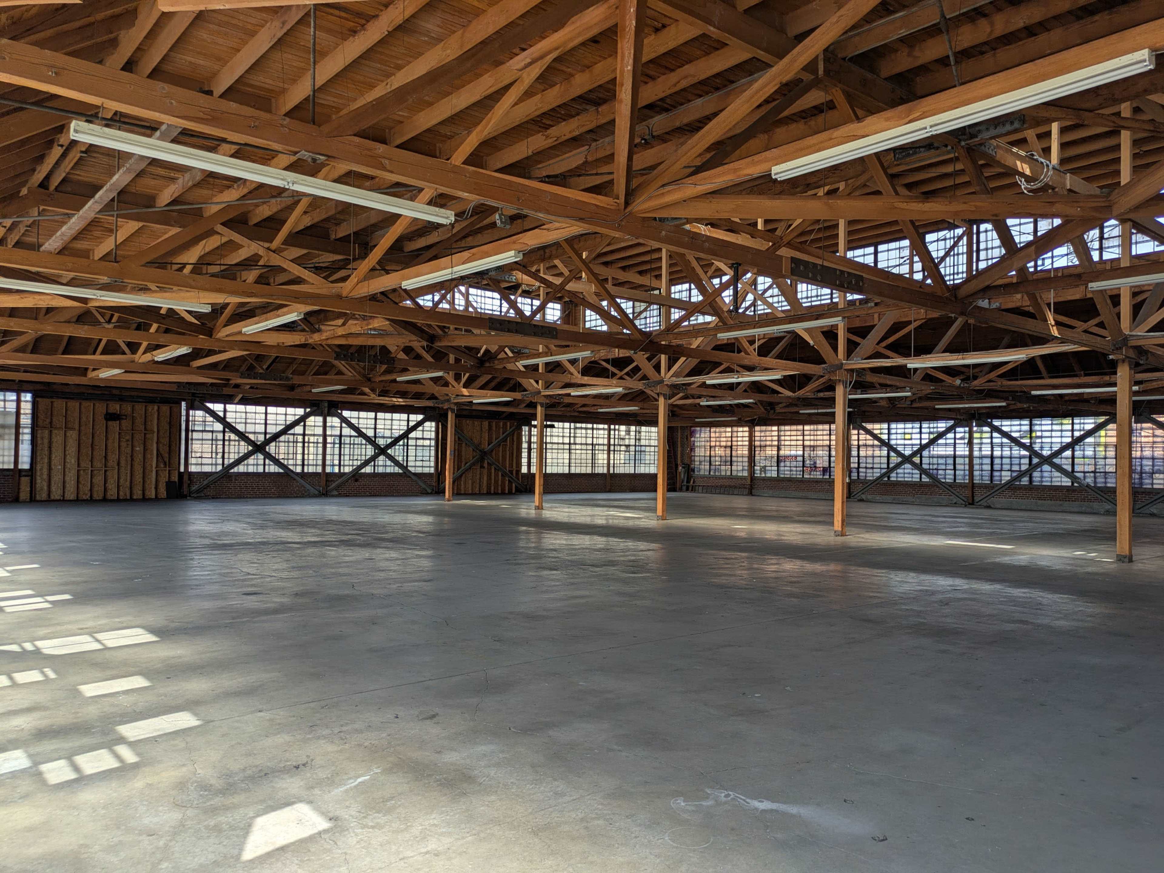 The image shows a spacious interior of a building with exposed wooden beams and large windows, creating a bright, open environment.