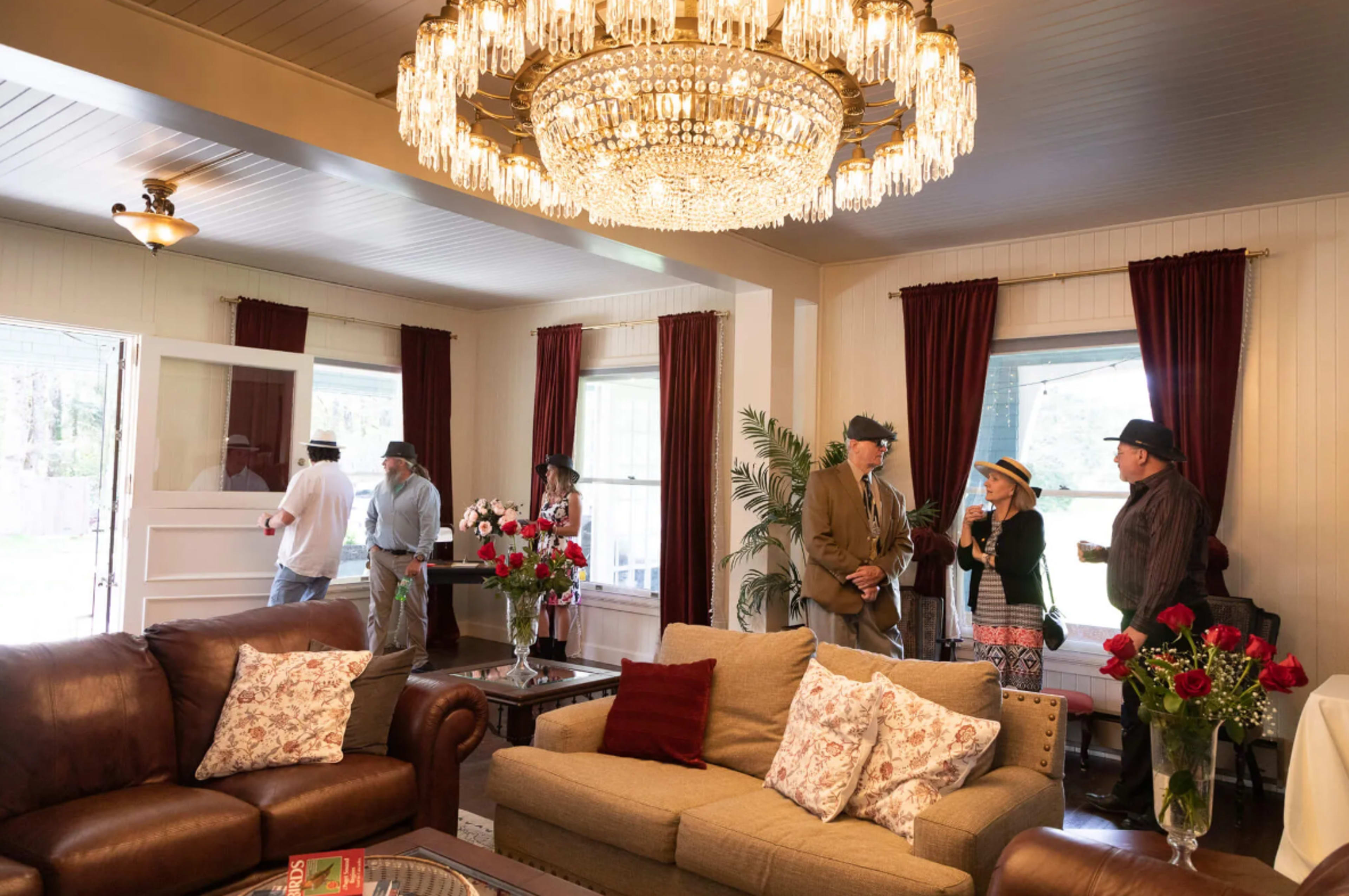 A group of people socializes in a living room adorned with elegant decor and a large chandelier.