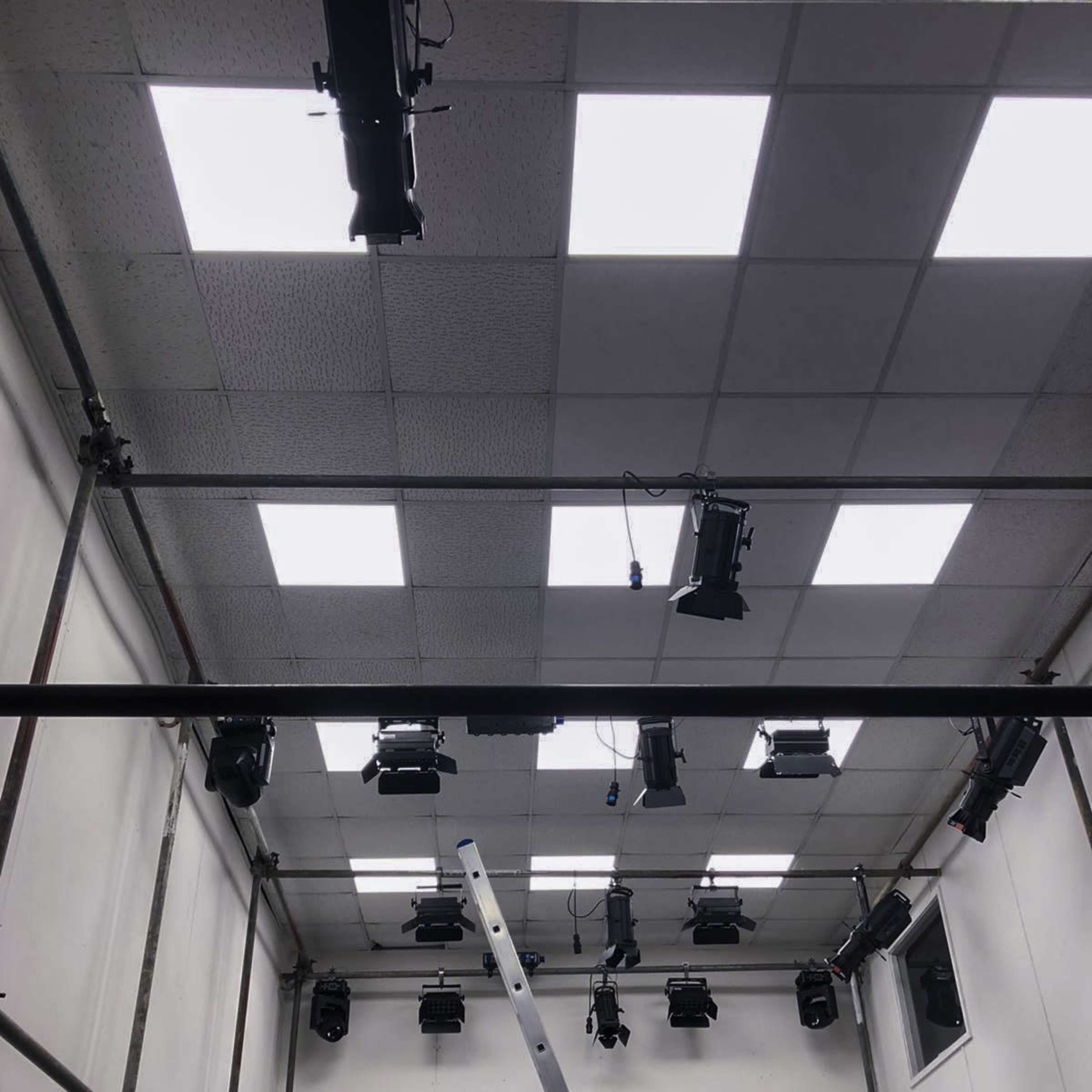 A room's ceiling with multiple stage lights installed on a grid above a ladder.
