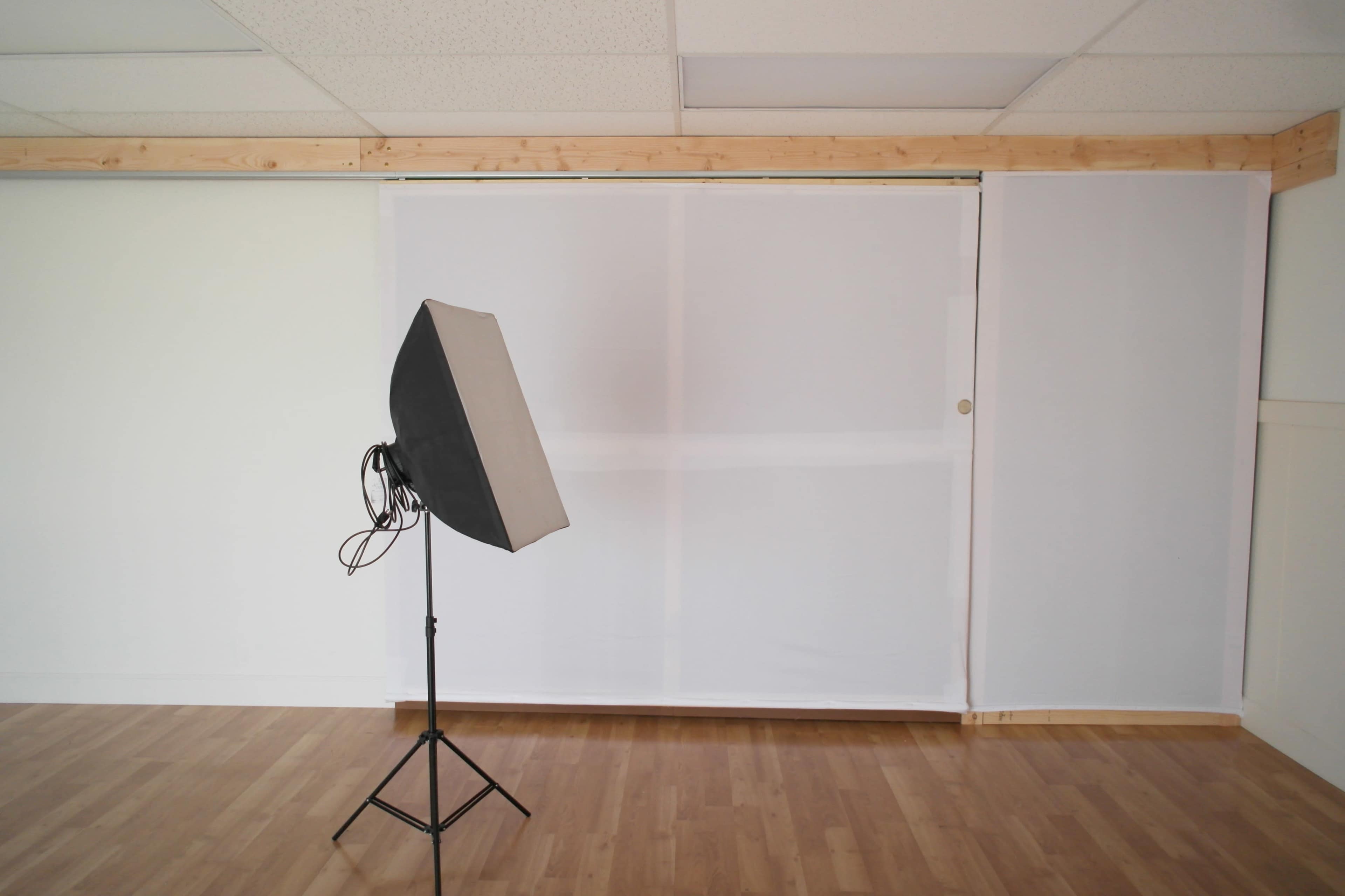 A photography studio features a softbox light positioned in front of a white backdrop and wooden paneling.