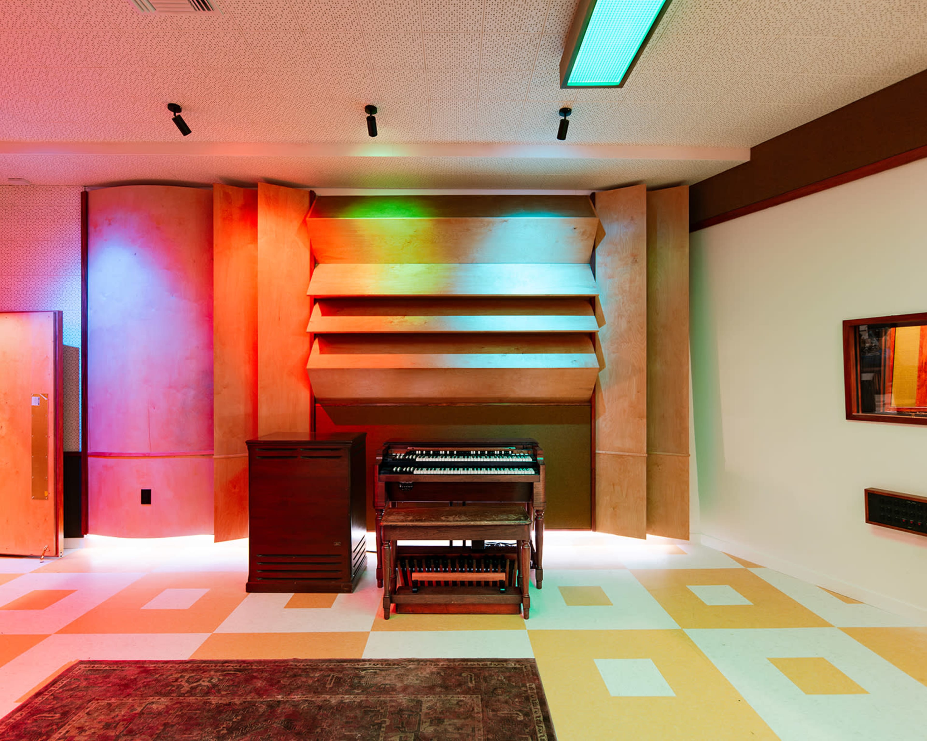 A room with illuminated wooden wall panels, a vintage organ, and colorful floor tiles.