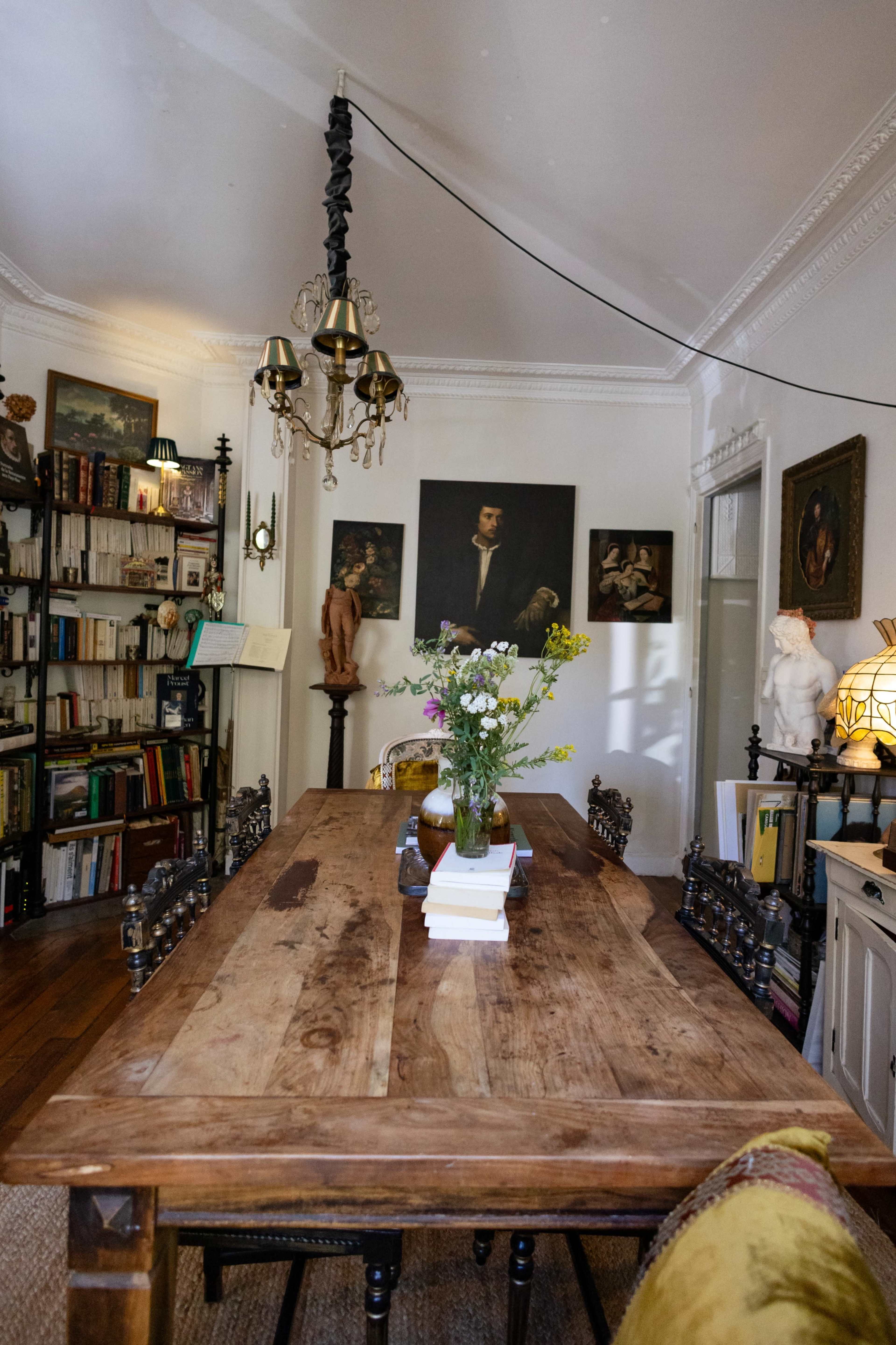 A wooden dining table is centered in a room filled with bookshelves, artwork, and decorative items.