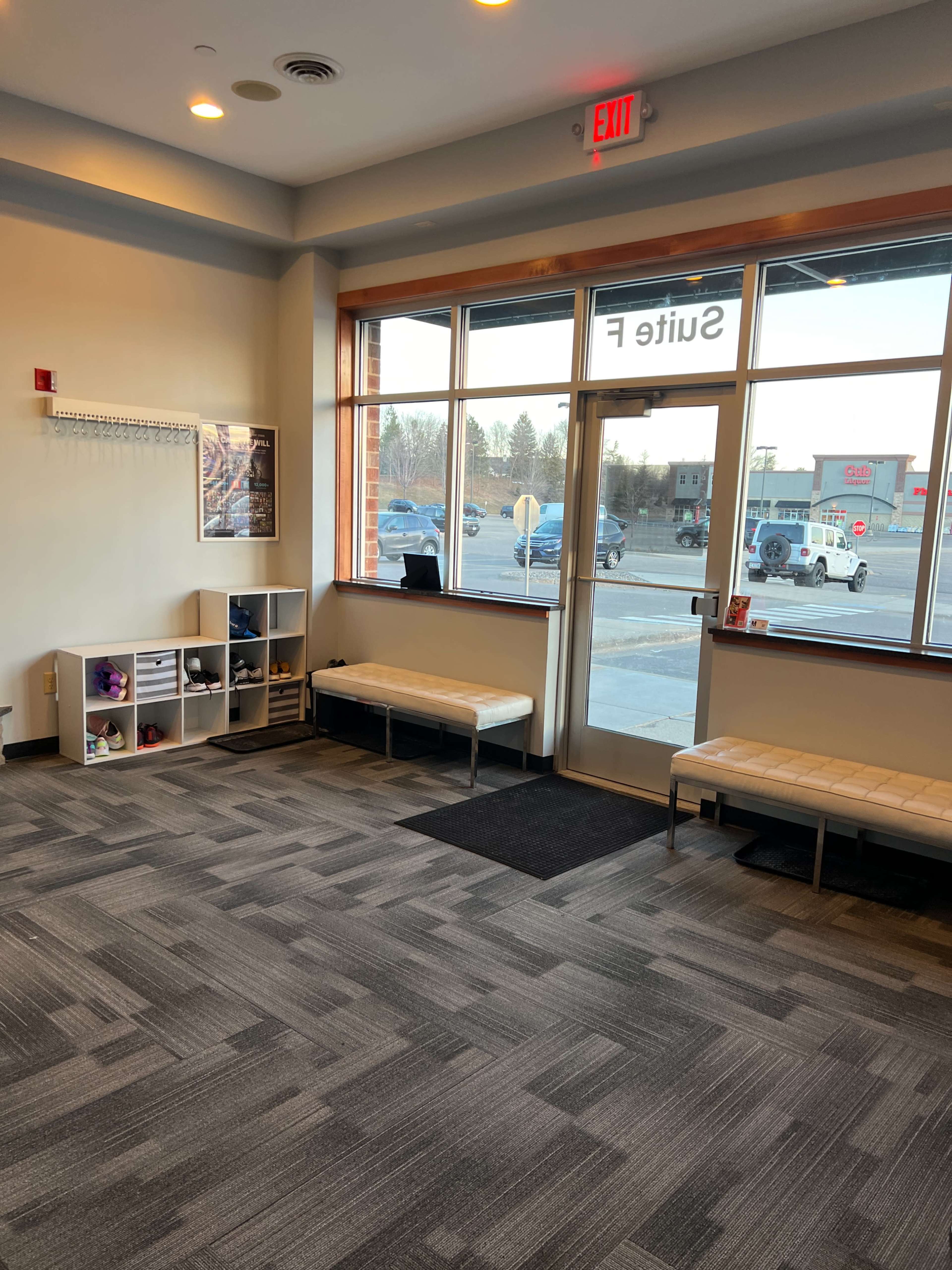 A spacious lobby area with a bench, shelving units, and large windows facing a parking lot.