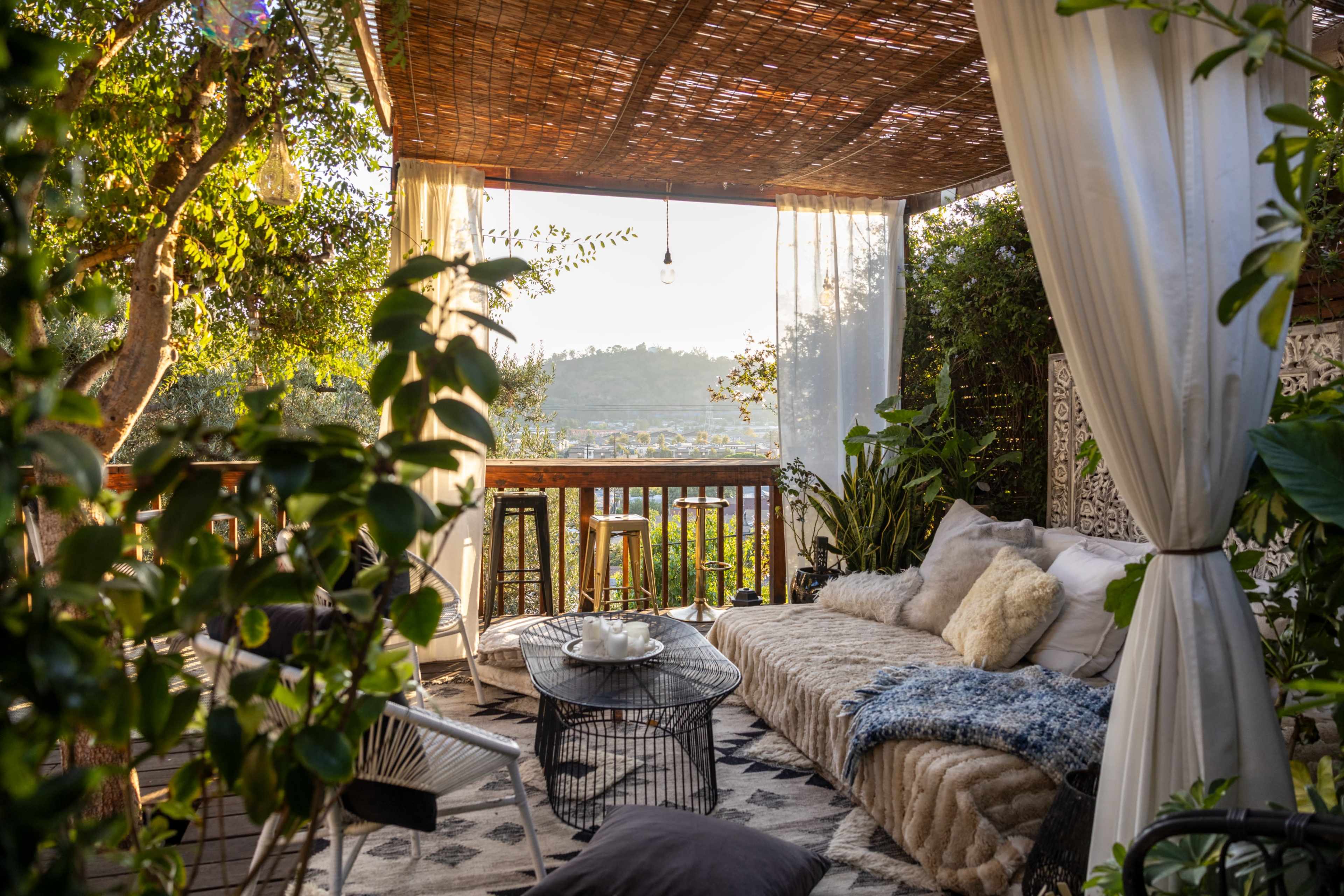 A cozy outdoor seating area with a couch, table, and plants, surrounded by a bamboo canopy and overlooking a scenic view.