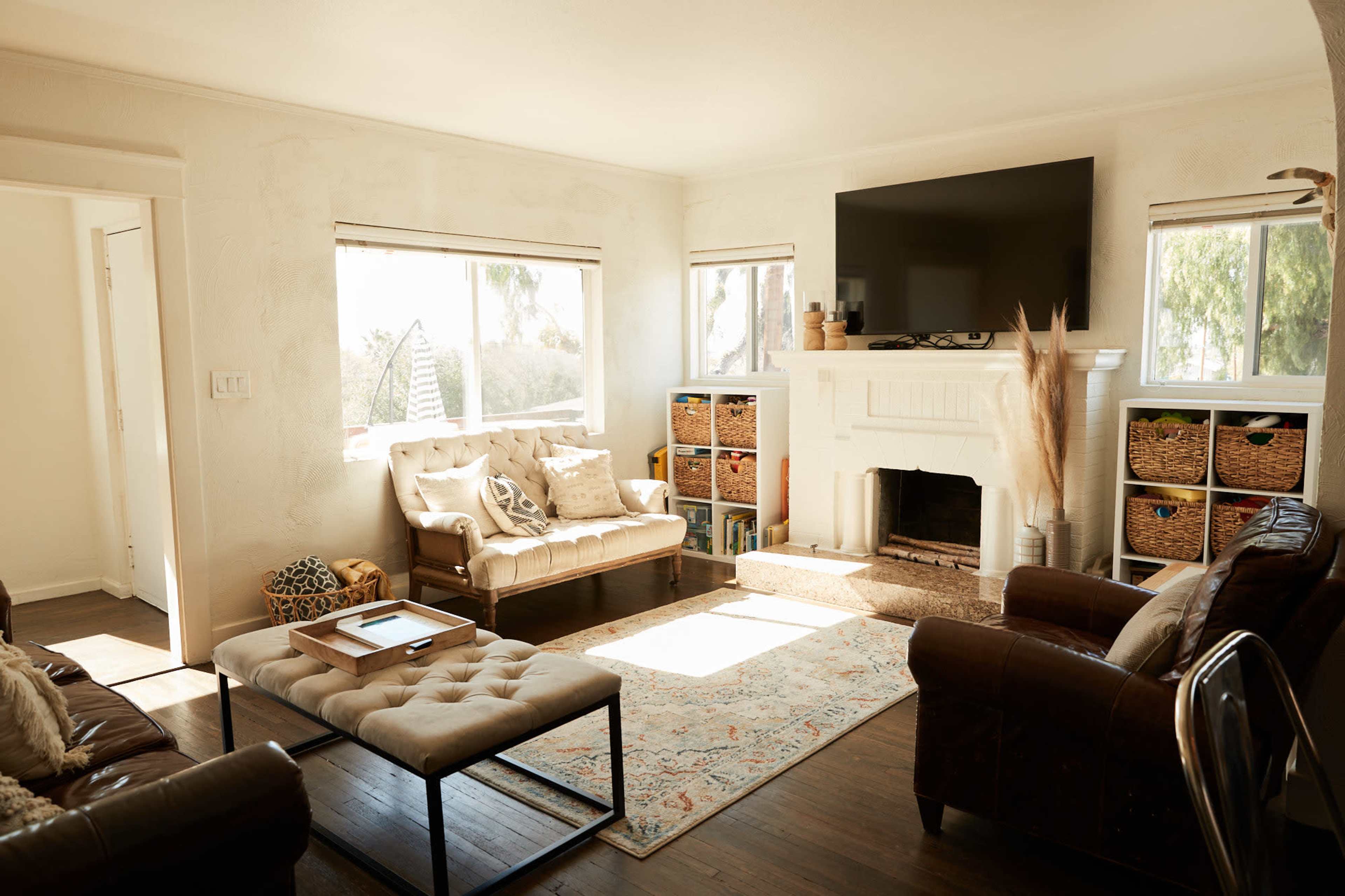 A living room features two sofas, a coffee table, a fireplace with a large television above it, and shelves filled with wicker baskets.