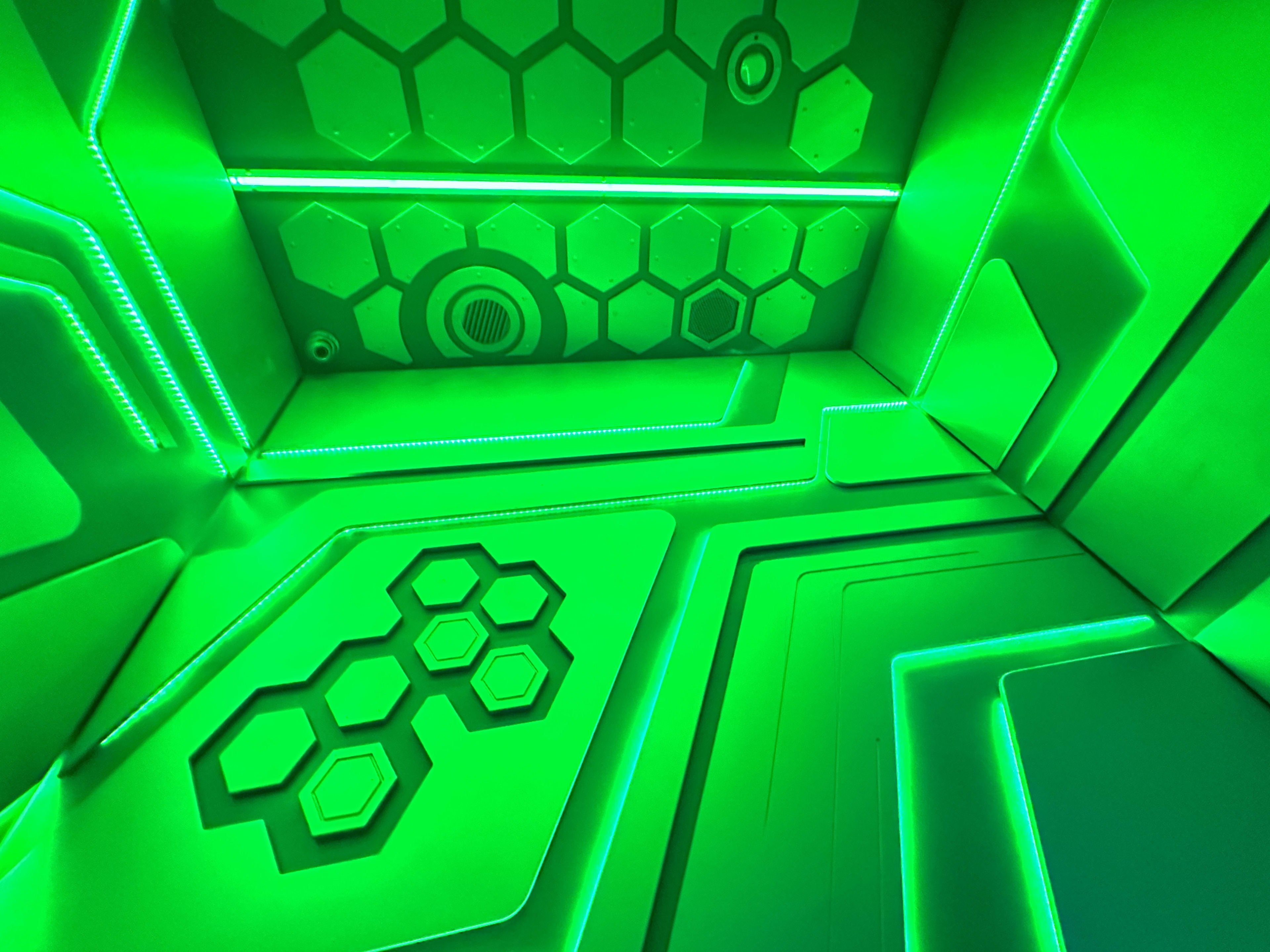 The image shows a room with hexagonal patterns and glowing green LED lights along the walls and ceiling.