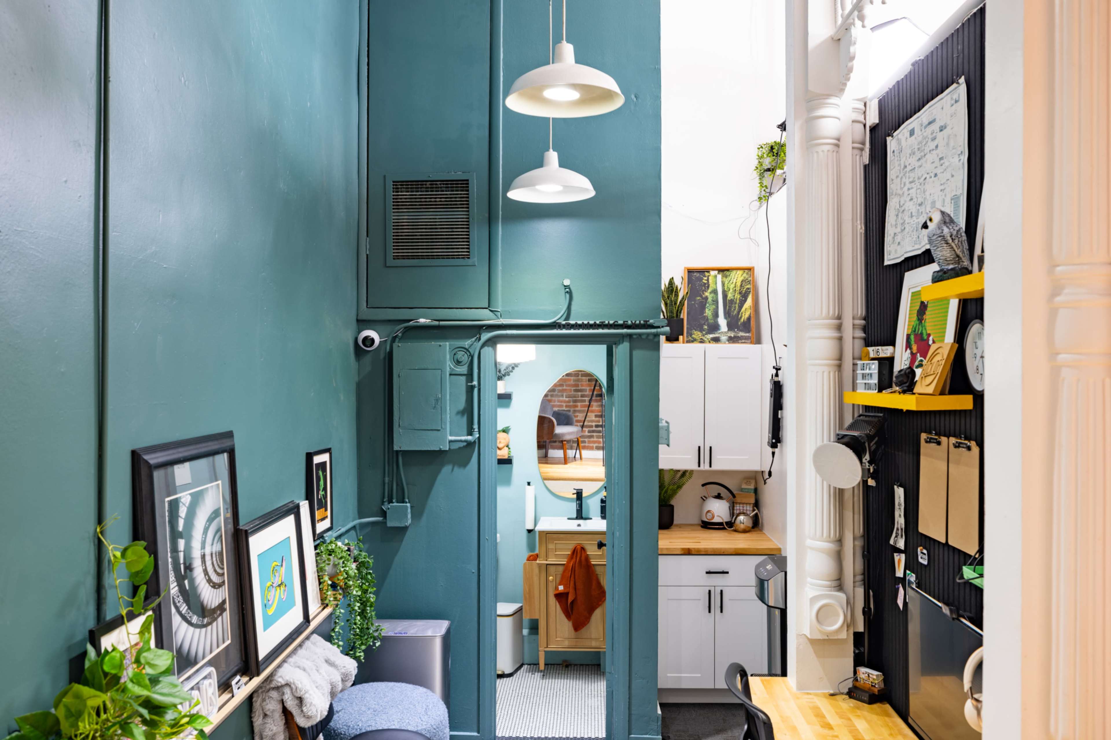 The image shows a narrow corridor leading to a bathroom, with green walls and a kitchen area visible at the end, featuring bright decor and organized shelving.