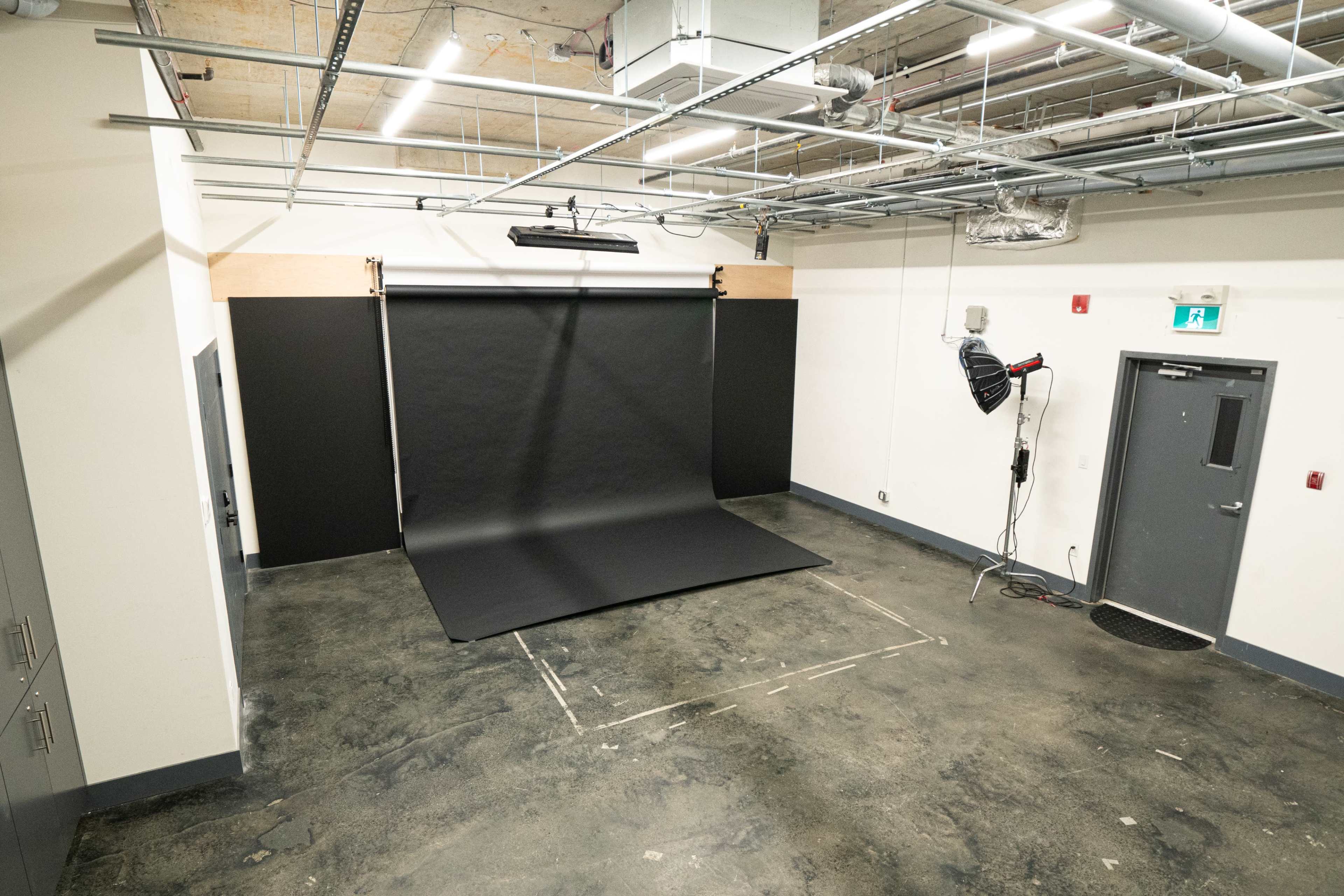 A photography studio with a black backdrop, lit by overhead lights, and concrete flooring.