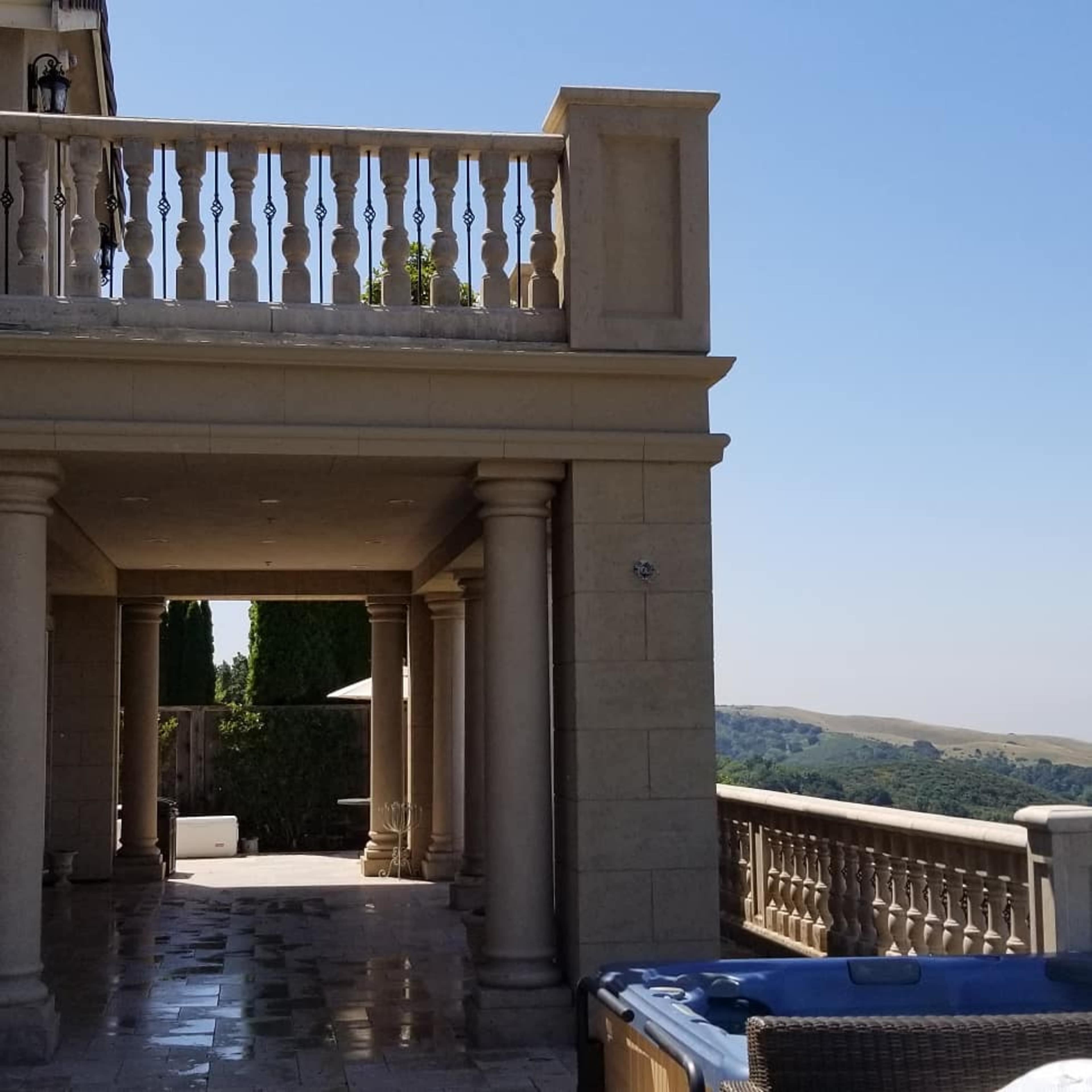 A stone patio with columns leads to a view of hills under a clear blue sky.