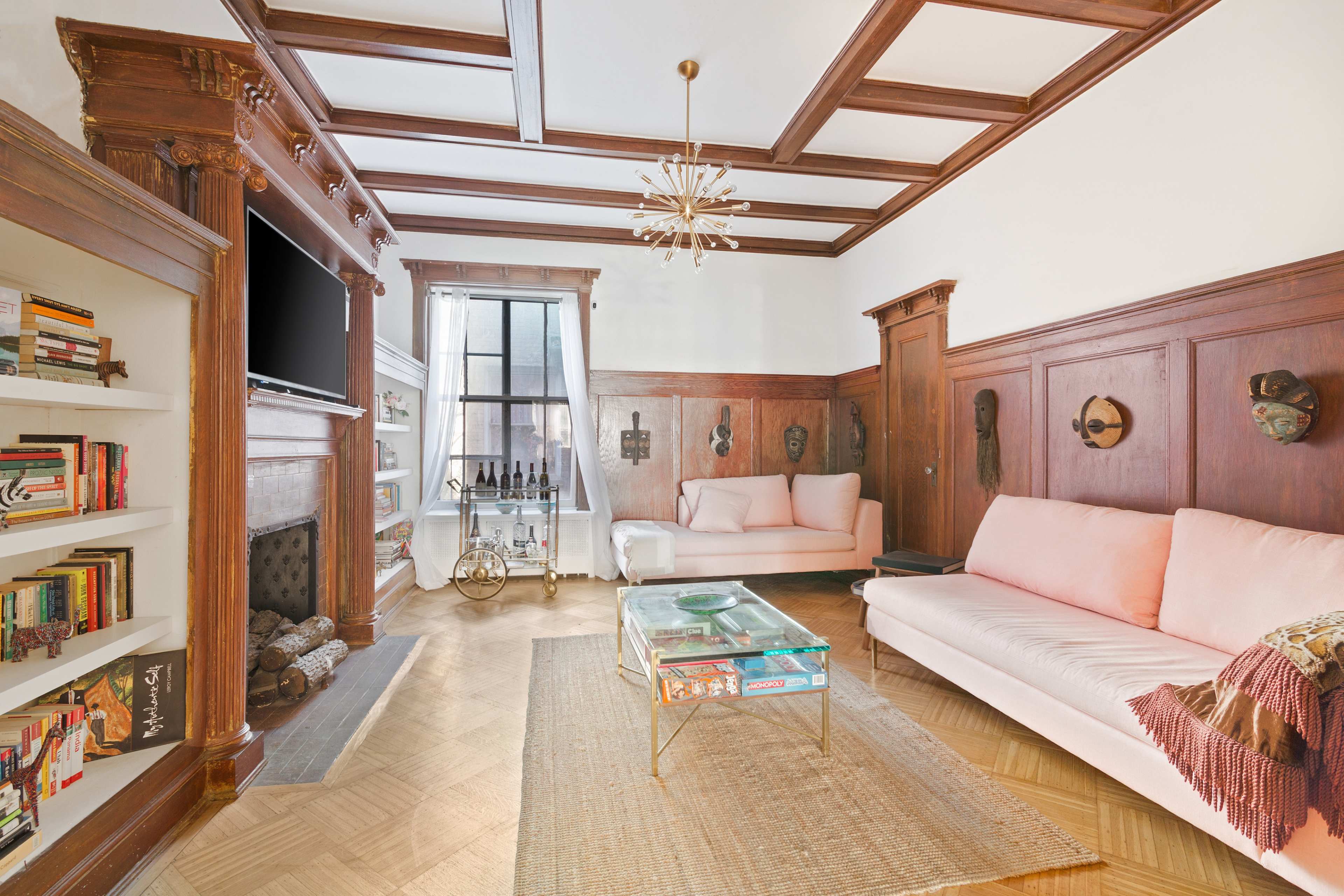 A living room features exposed wooden beams, a glass coffee table, and light pink sofas, with a bookshelf and a television mounted on the wall.