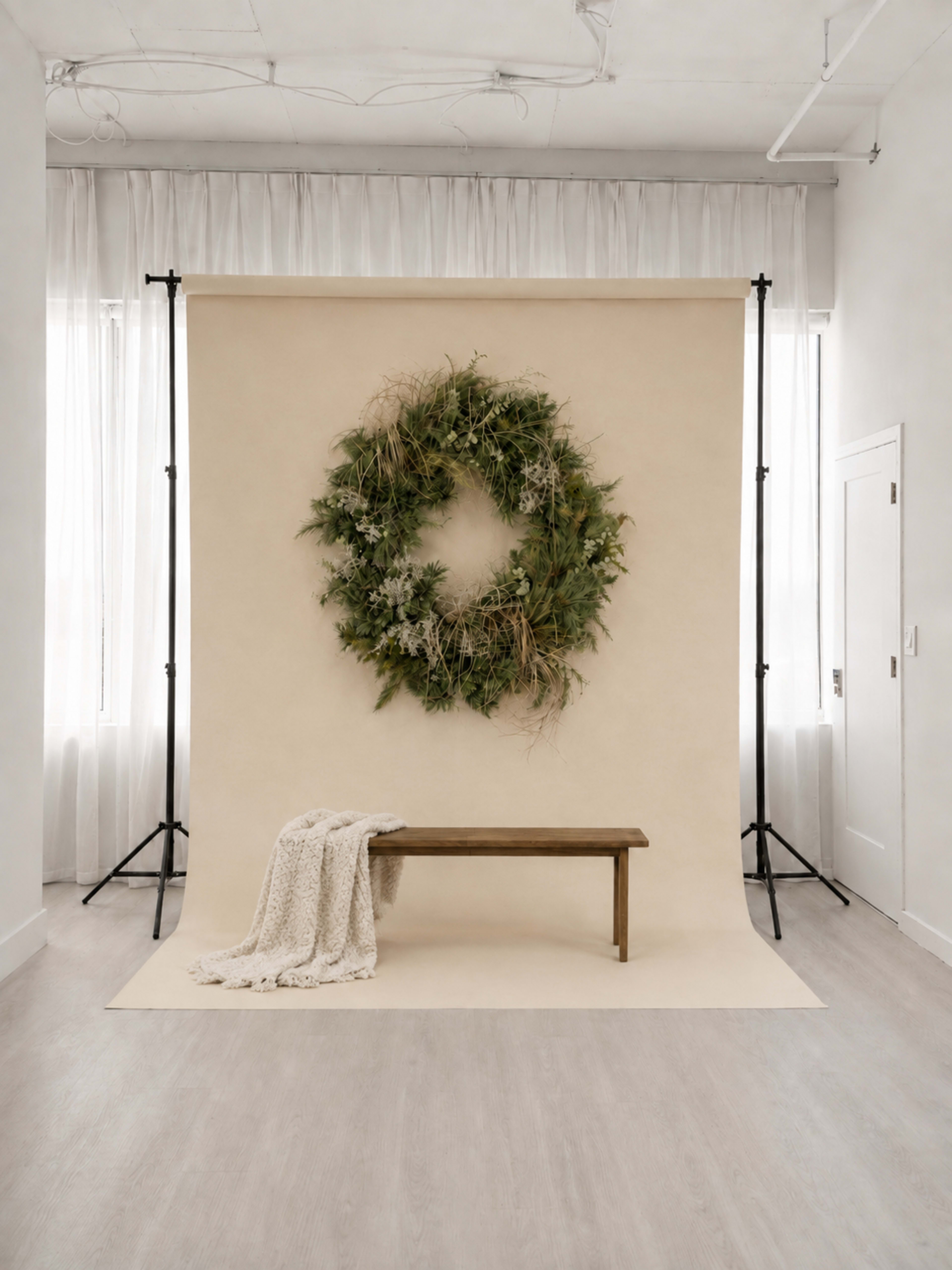 The image shows a wooden bench in front of a large circular wreath hanging on a beige backdrop in a well-lit indoor setting.