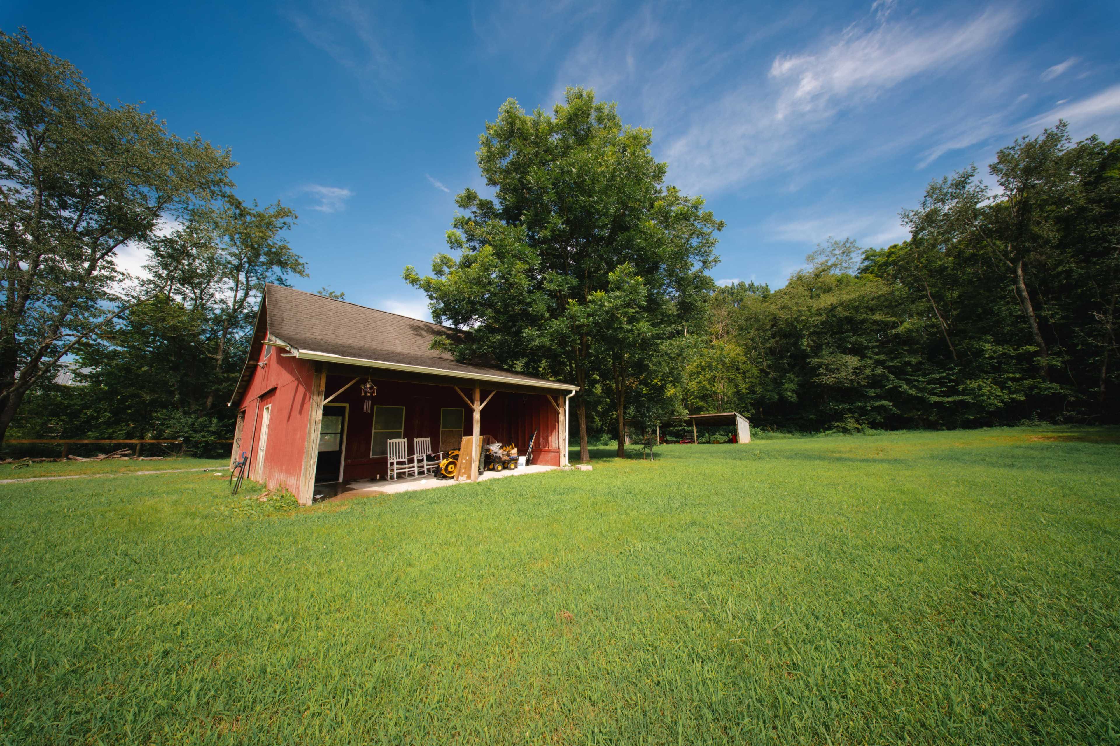 A red barn stands in a green field surrounded by trees under a blue sky.