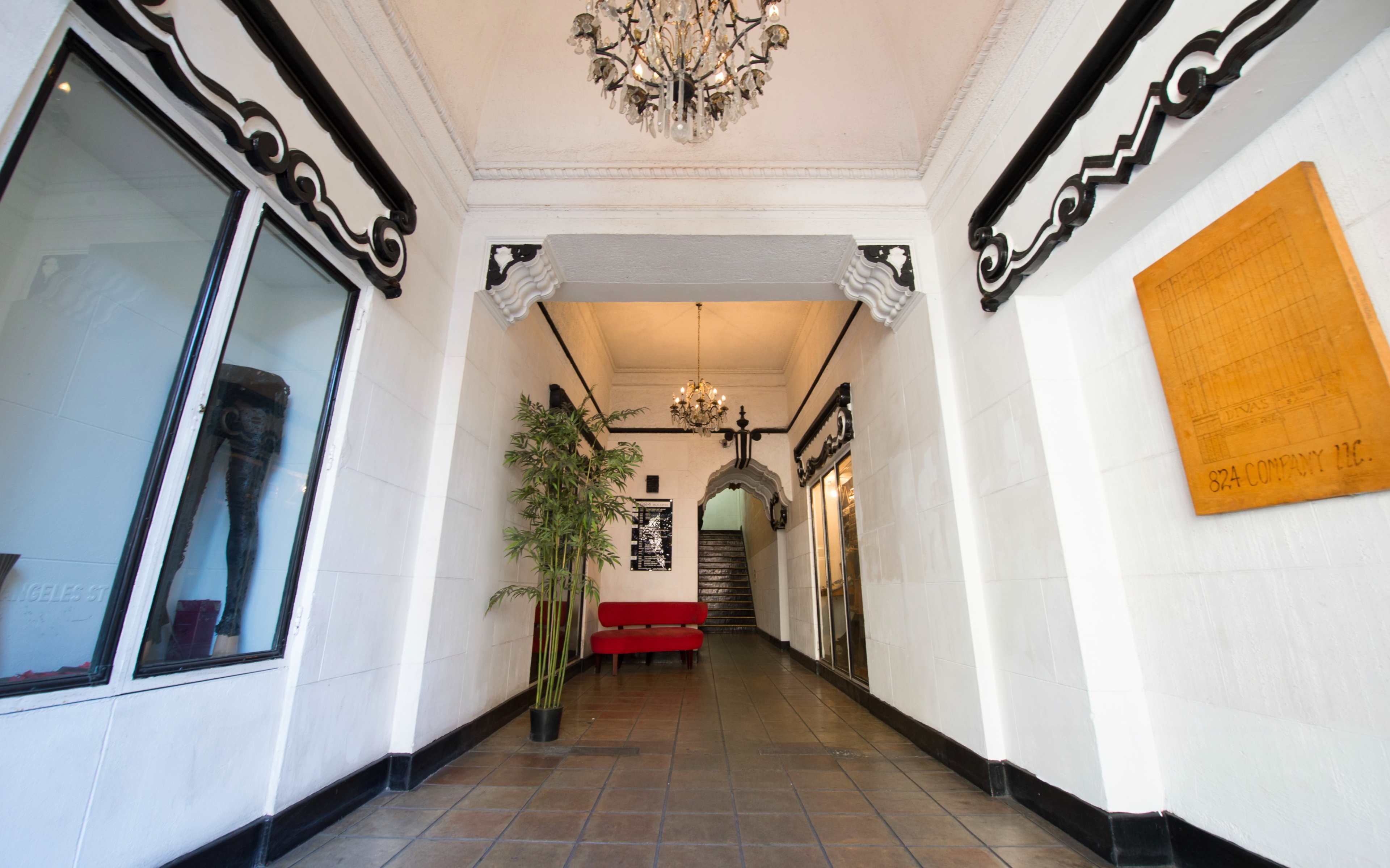 A hallway with a chandelier, a red couch, bamboo plants, and an ornate ceiling leading to a staircase.
