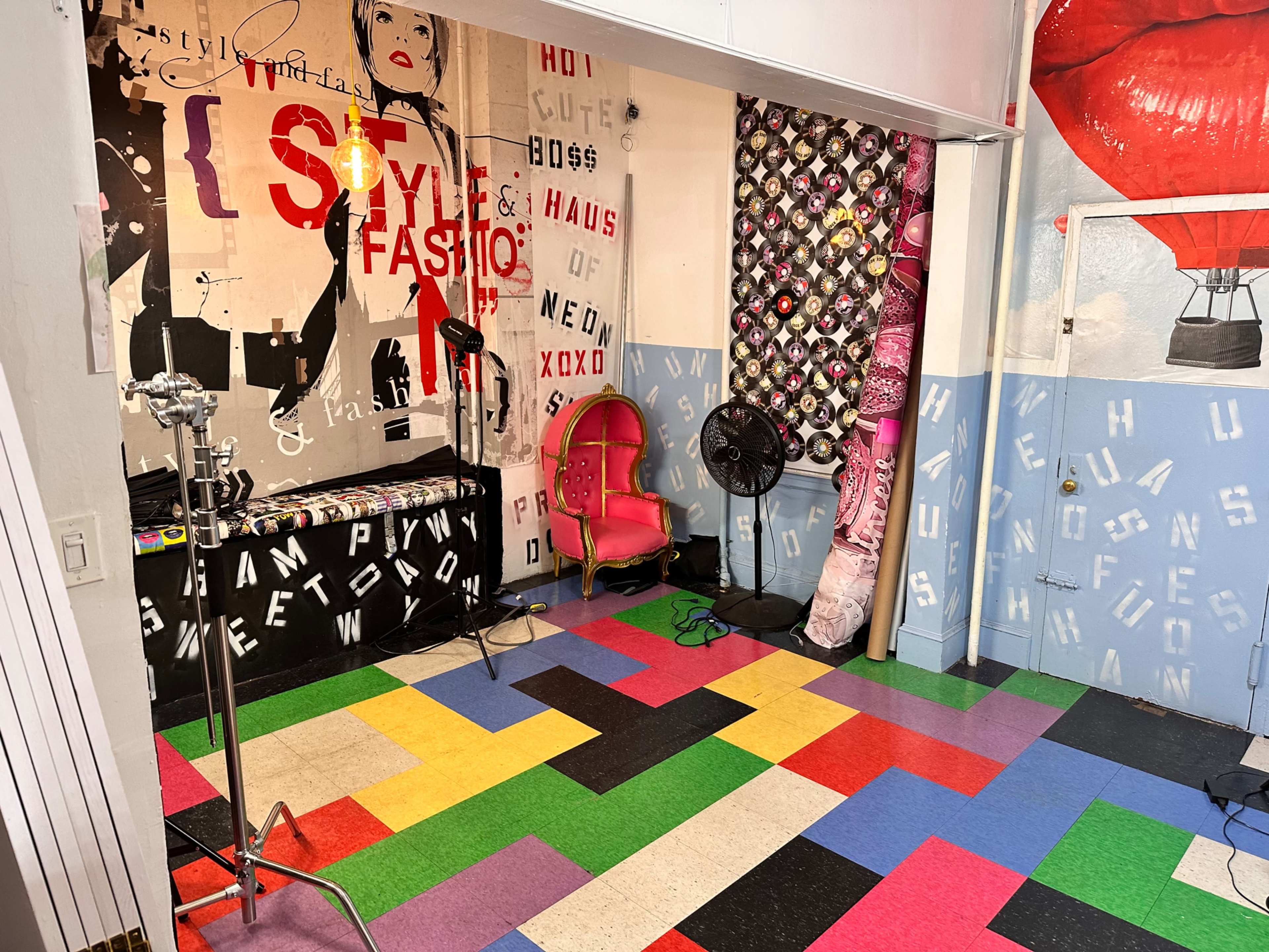 A colorful studio space with a pink chair, lighting equipment, and walls adorned with art and vinyl records.