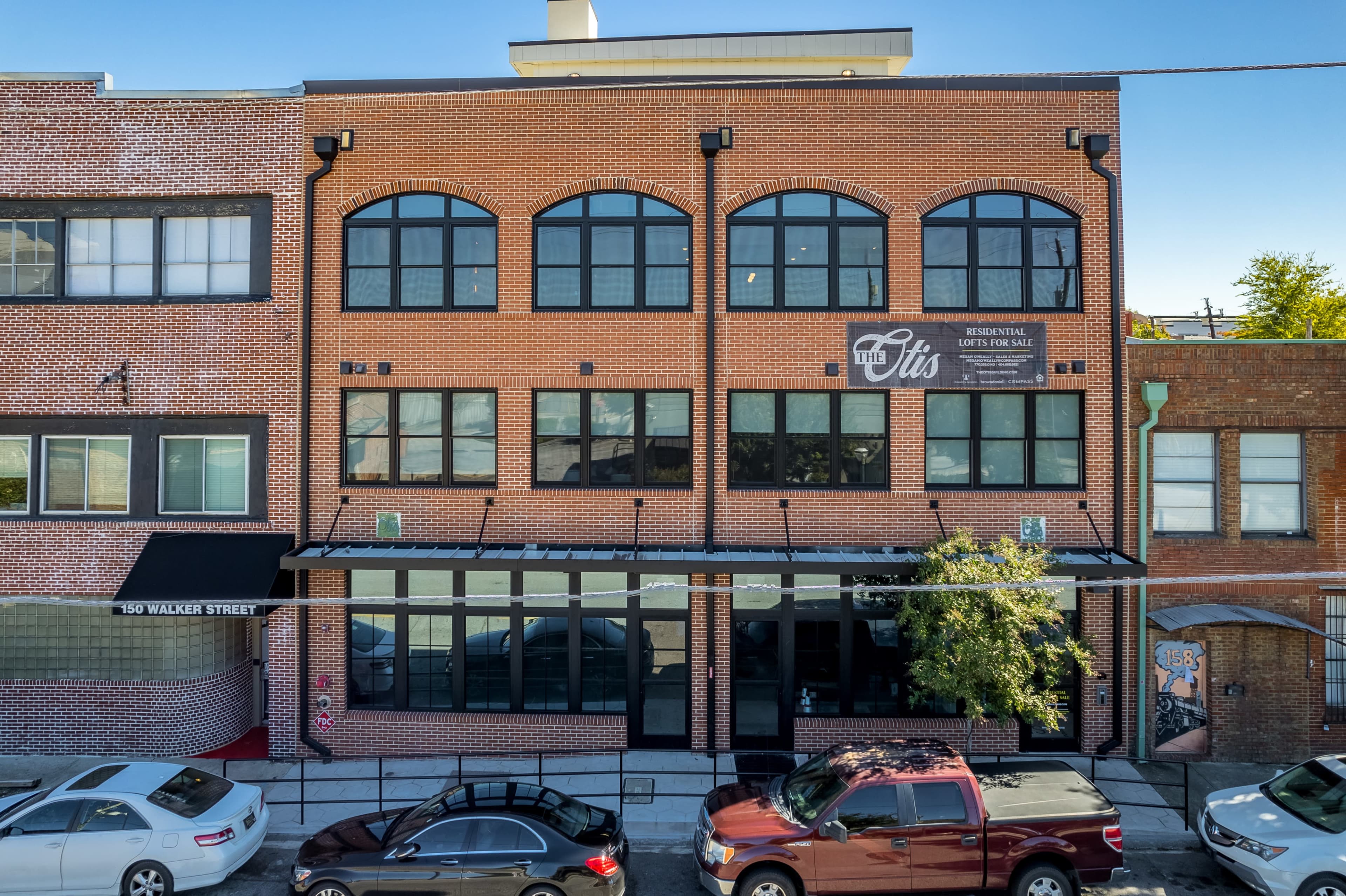 A red-brick building with large windows and a sign that reads "Otis," located on Walken Street, with parked cars on the street.