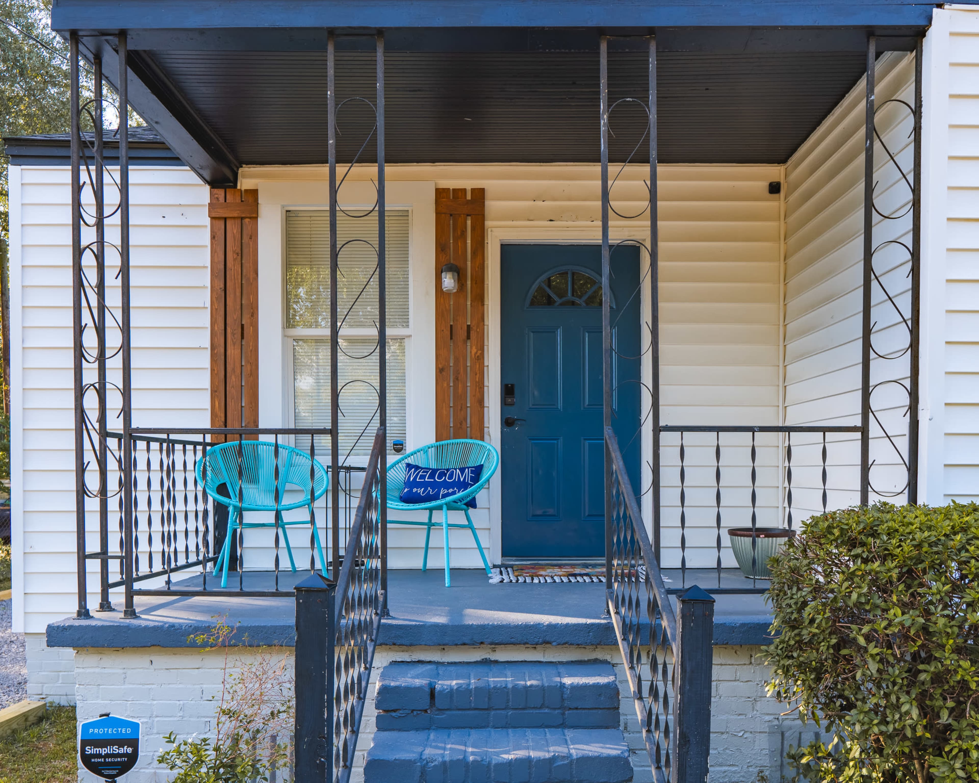 A welcoming porch with two teal chairs and a blue front door, flanked by decorative railings.