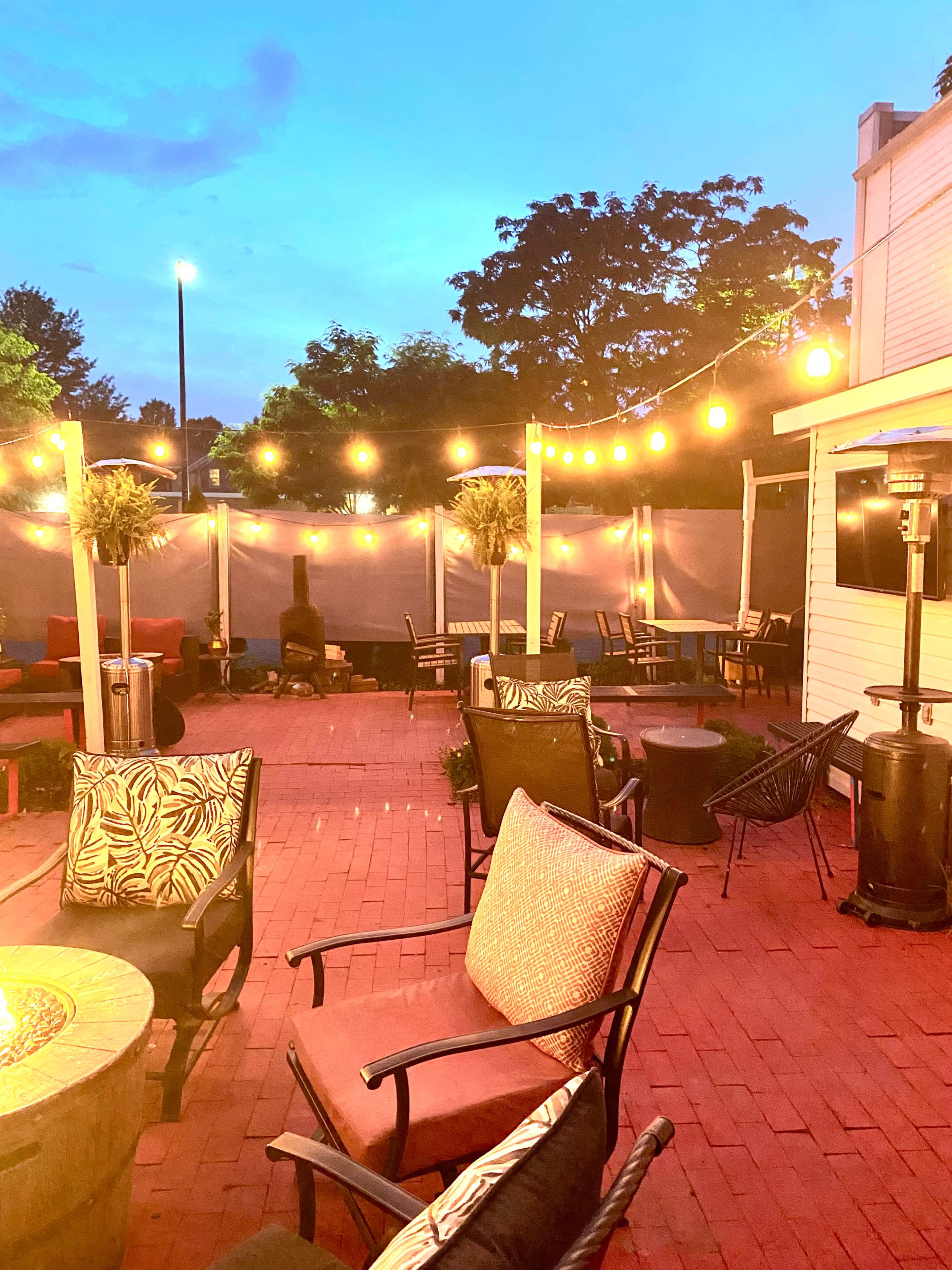 The outdoor patio features string lights overhead, along with various seating arrangements including chairs and tables on red brick flooring.