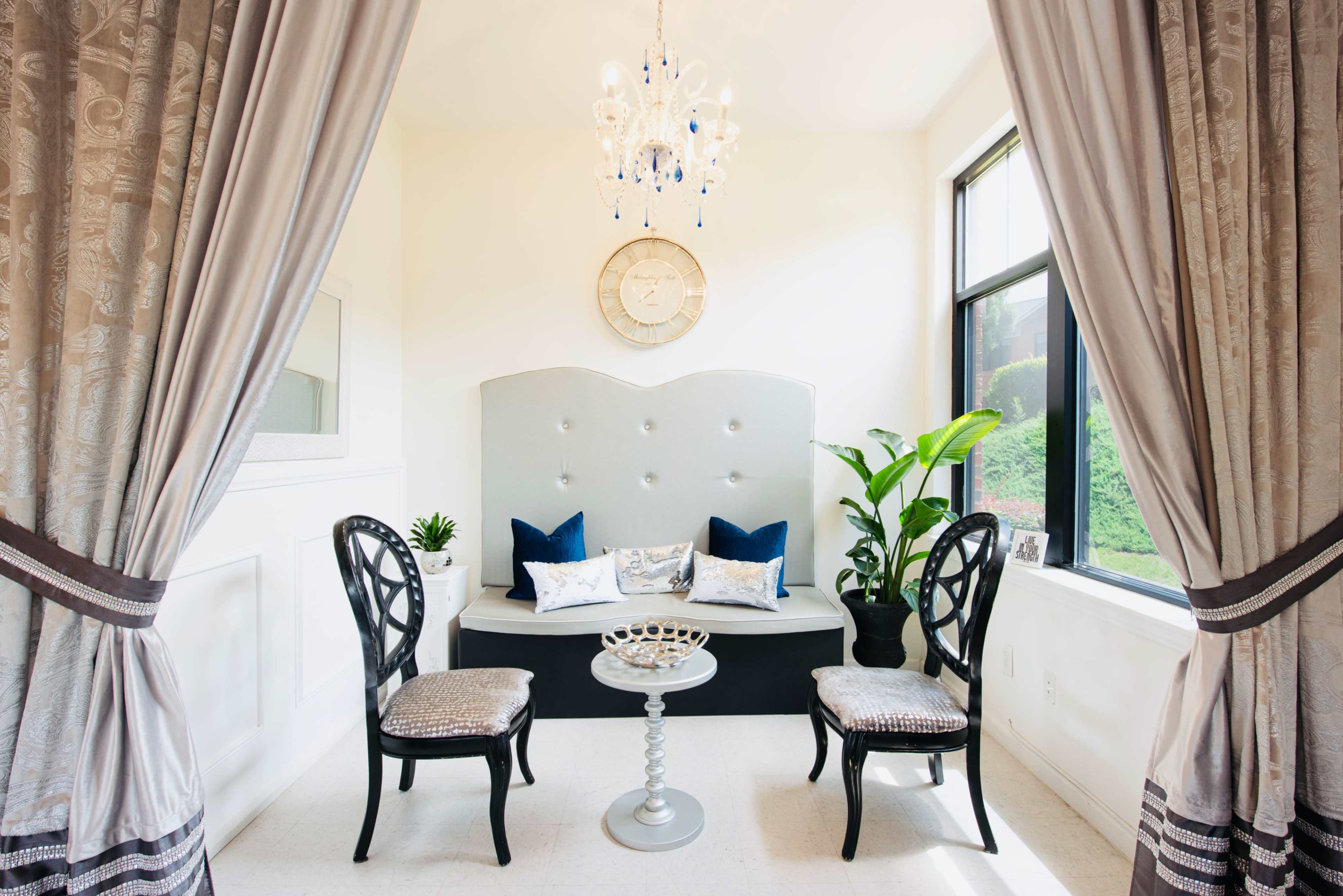 A small sitting area with a tufted gray bench, two black chairs, a round table, and a large window with nature visible outside.