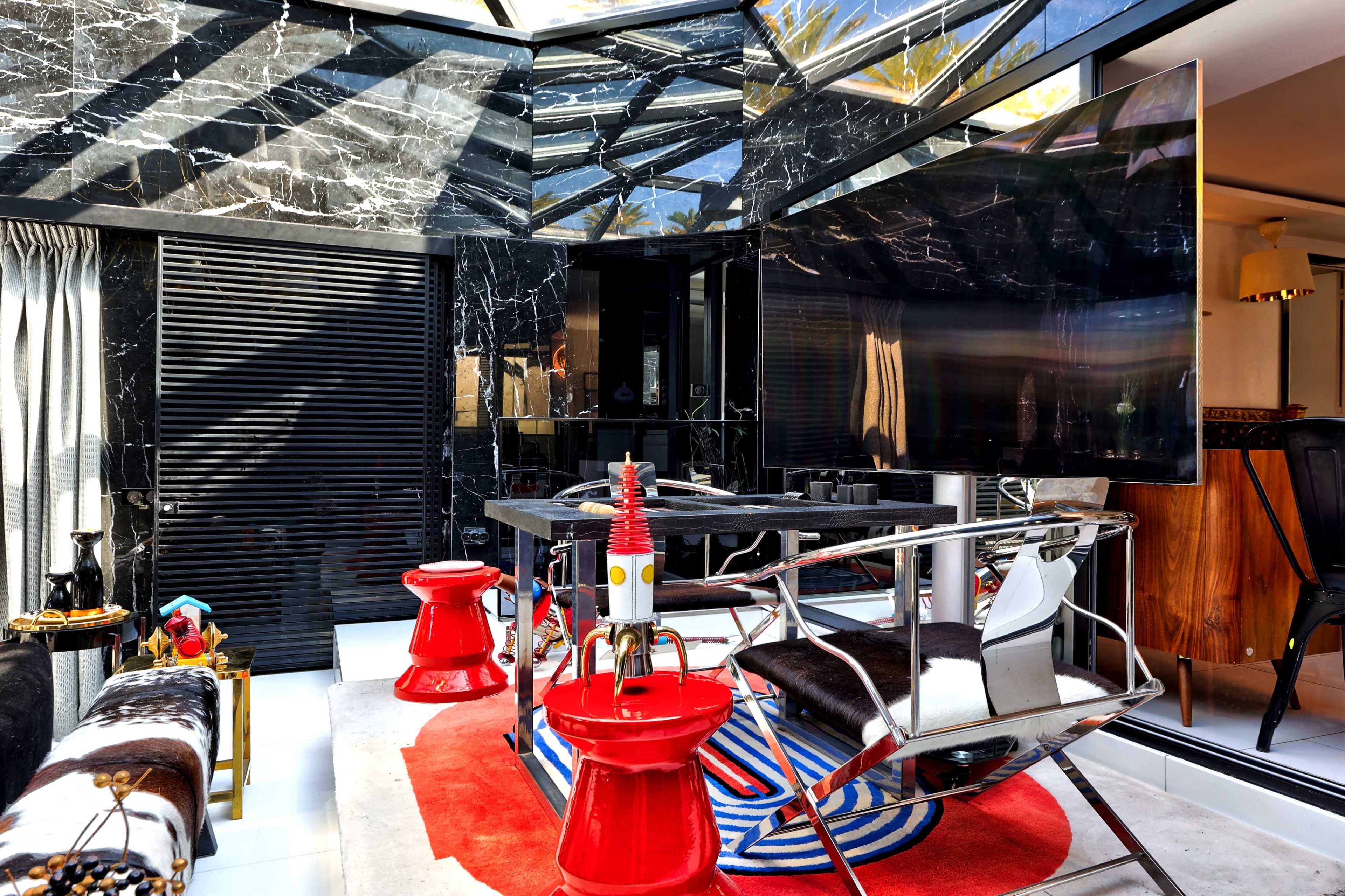 The image shows a modern interior space featuring a black marble wall, a large screen, and stylish furniture, including red stools and a circular rug.