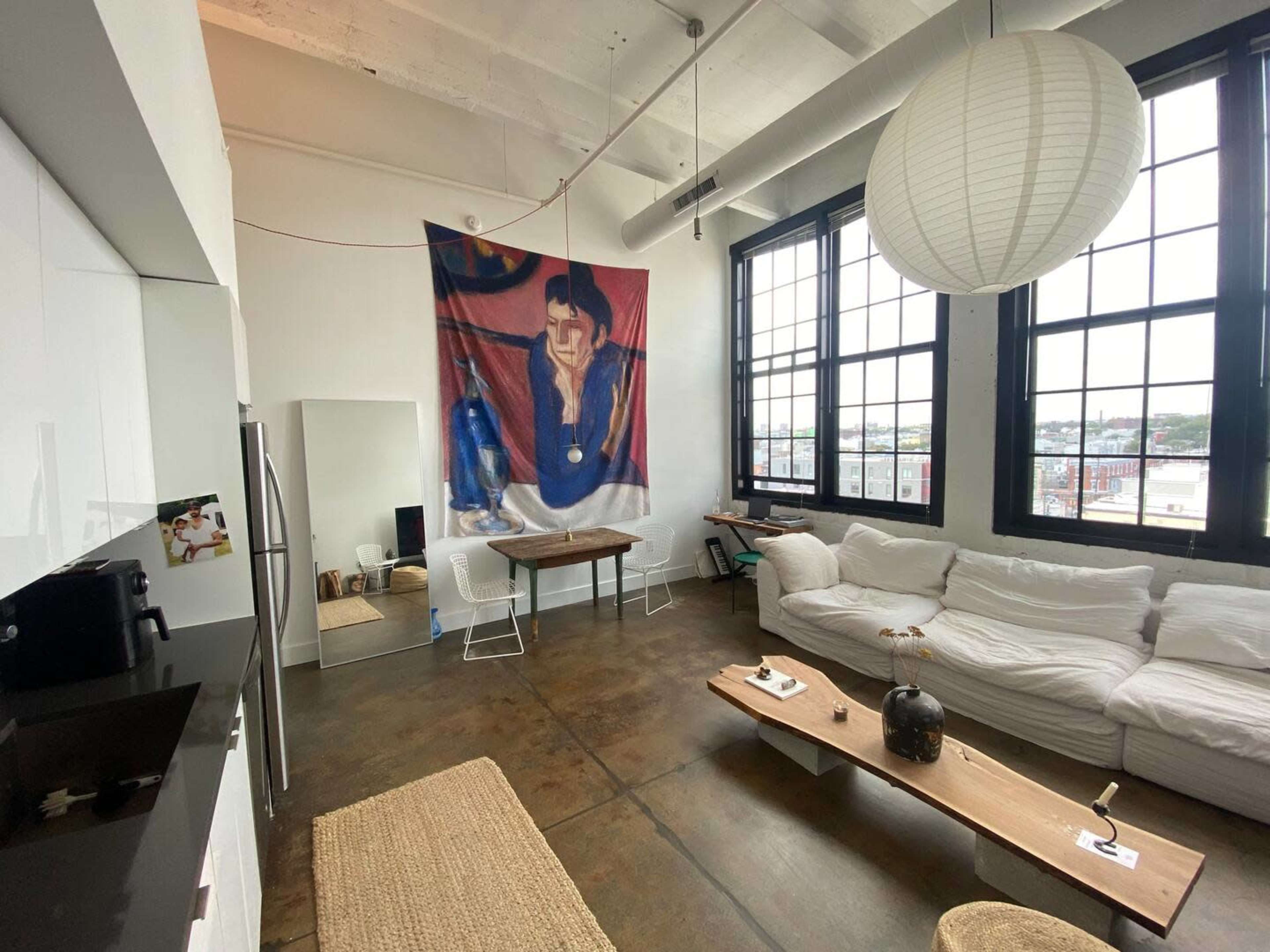 A modern loft features a spacious living area with a large banner hanging on the wall, a wooden table, a white couch, and large windows letting in natural light.