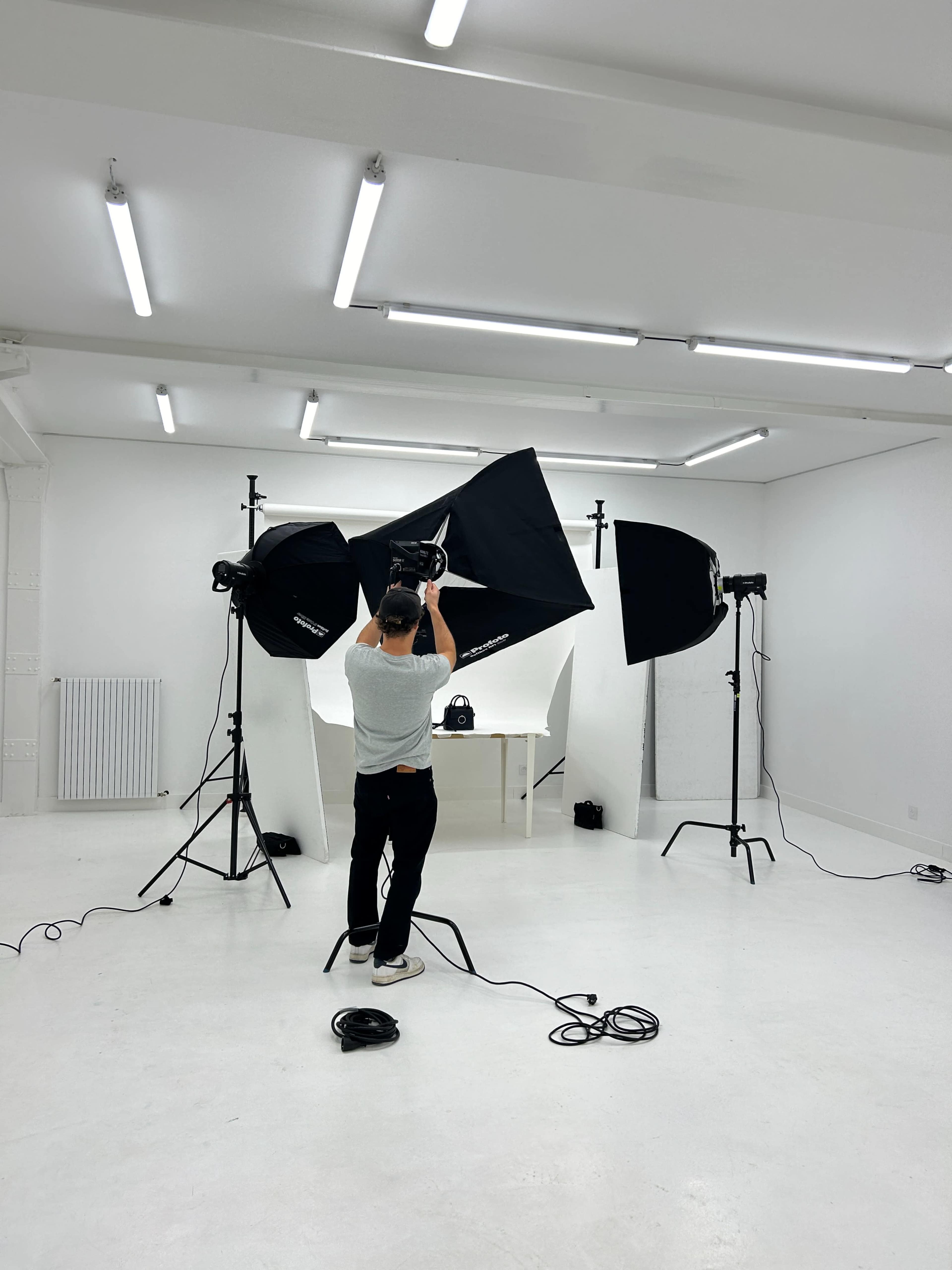 A person is setting up studio lighting equipment in a minimalist photography studio.