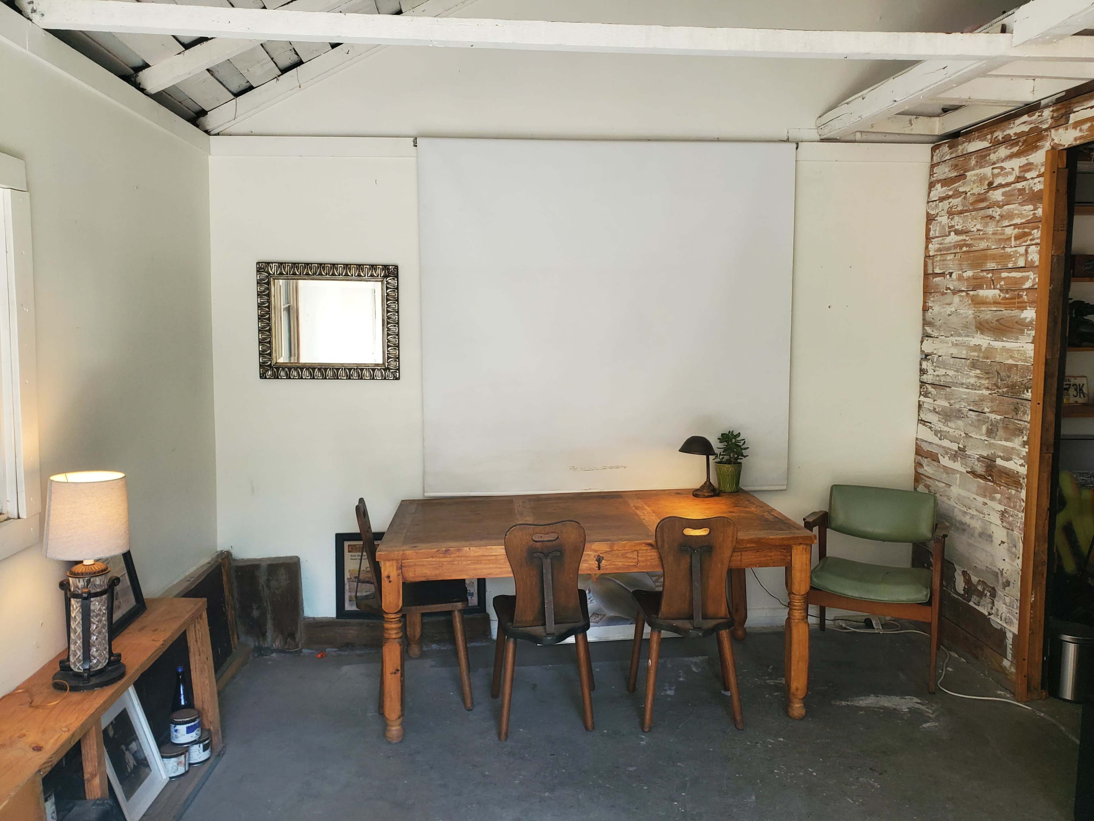 The image shows a simple room with a wooden table, four chairs, a lamp, and a blank white wall.