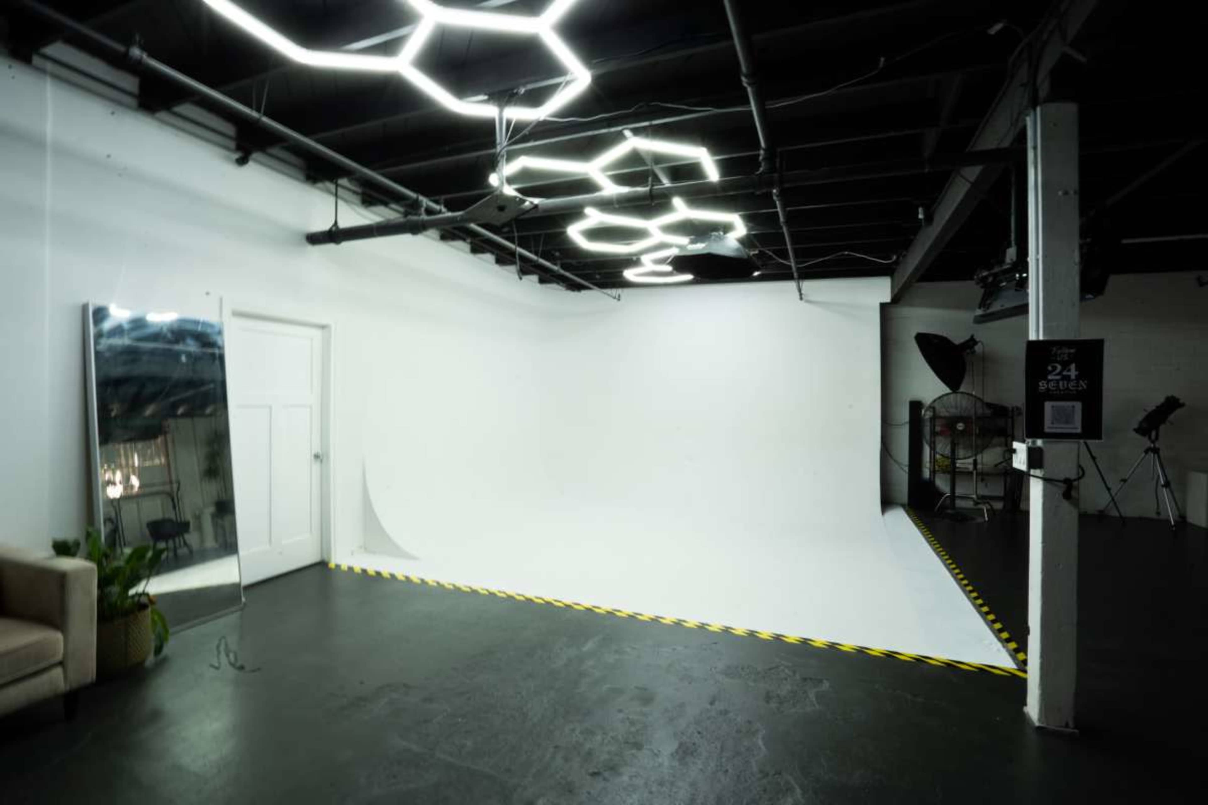 The image shows a spacious photography studio with a white backdrop, a large mirror, and hexagonal ceiling lights.